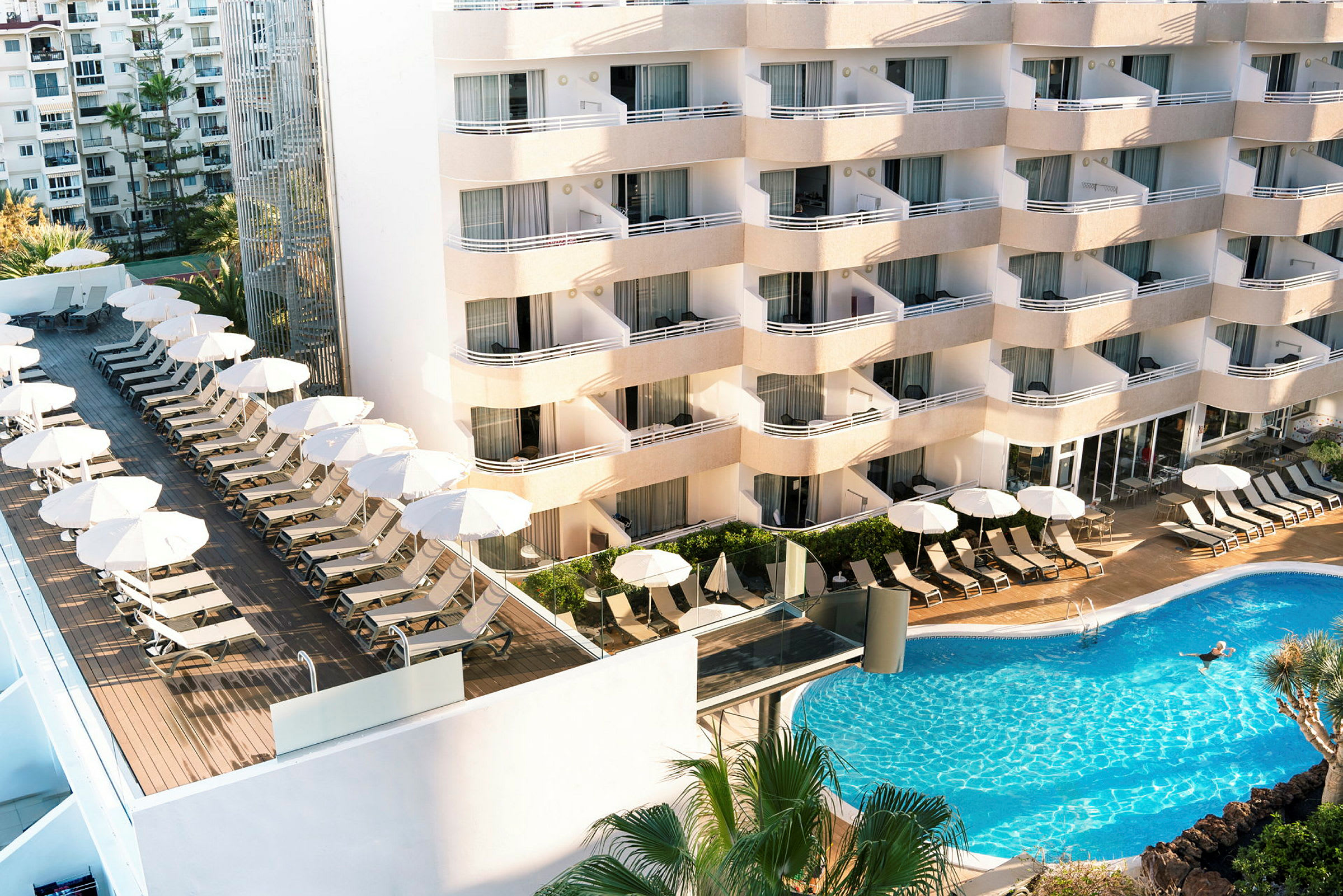 Billede af hotel med liggestole, parasoller og pool. (AI-genereret tekst)