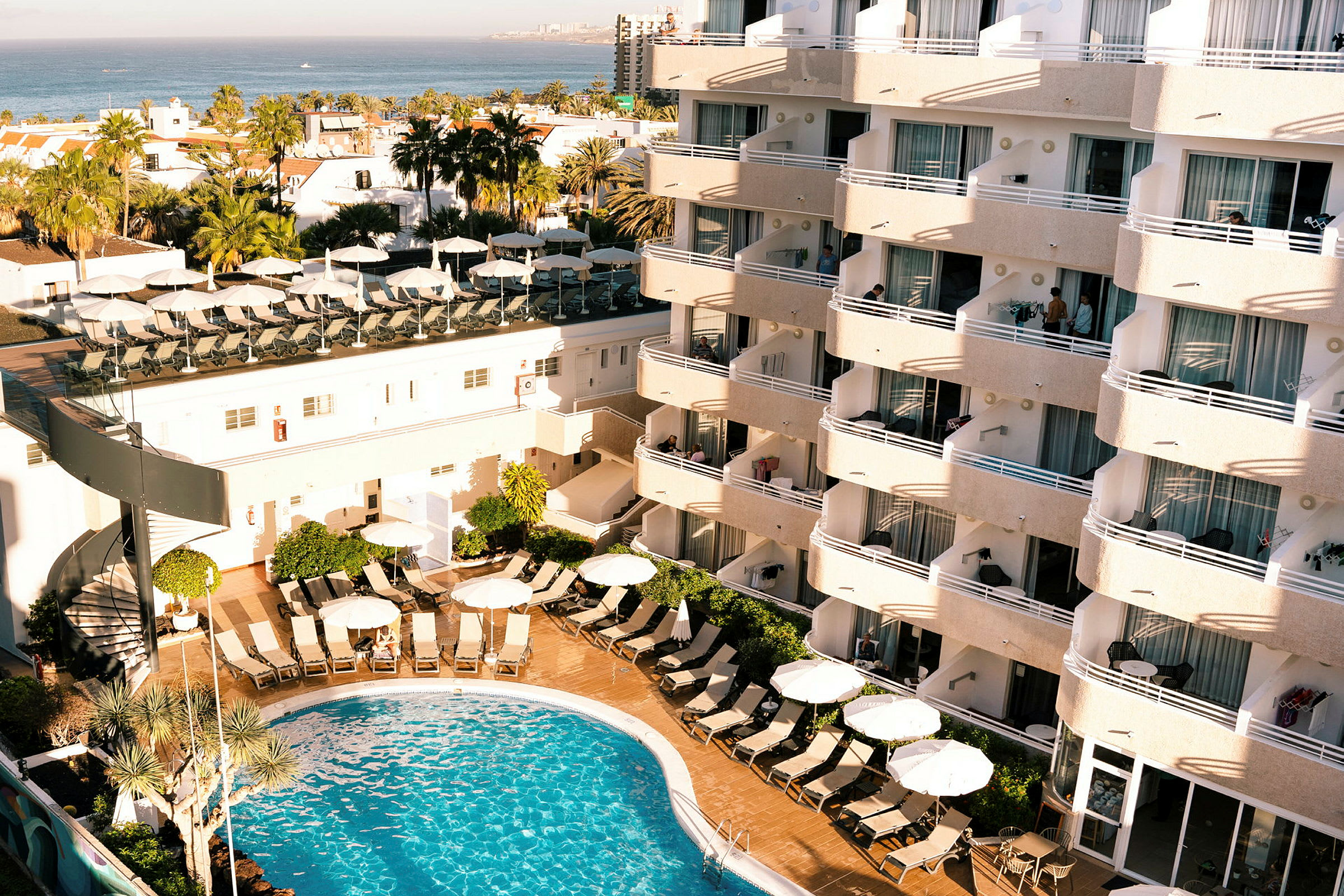 Hotelbygning med altaner og en pool i forgrunden. (AI-genereret tekst)