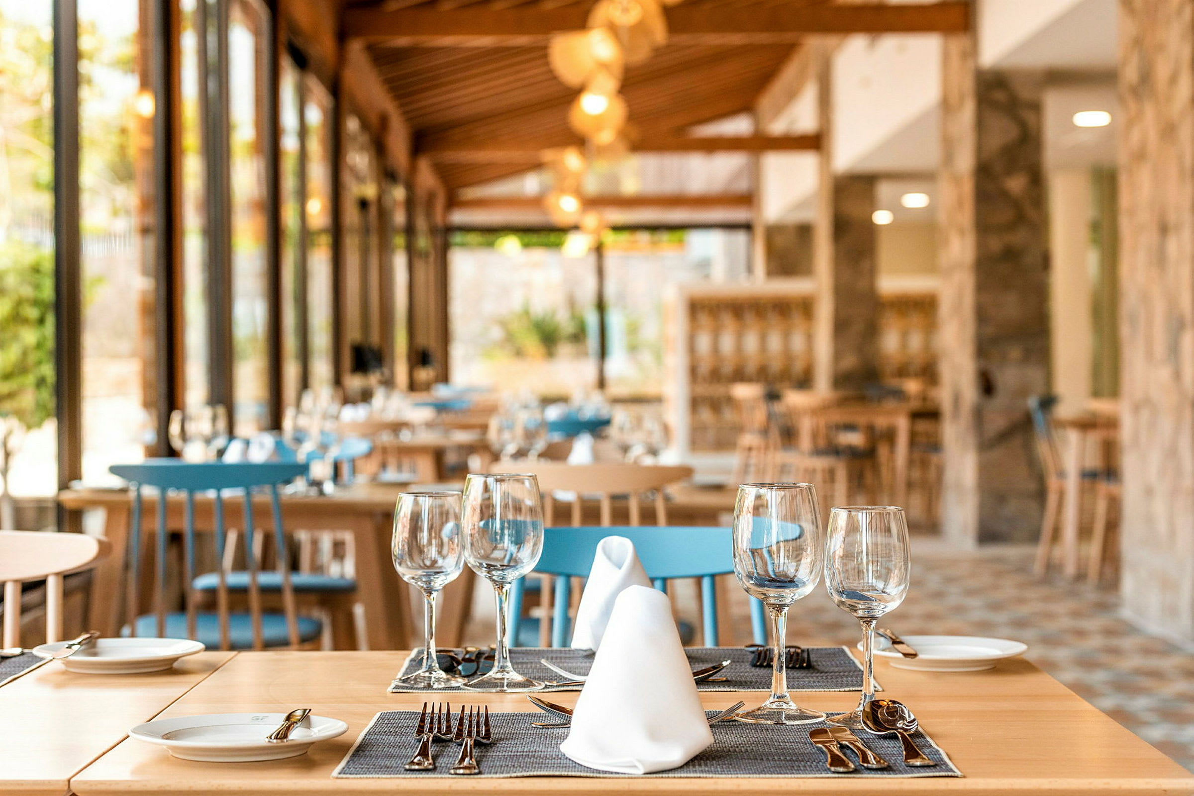 En elegant restaurant med træinteriør, dækkede borde og blå stole. (AI-genereret tekst)