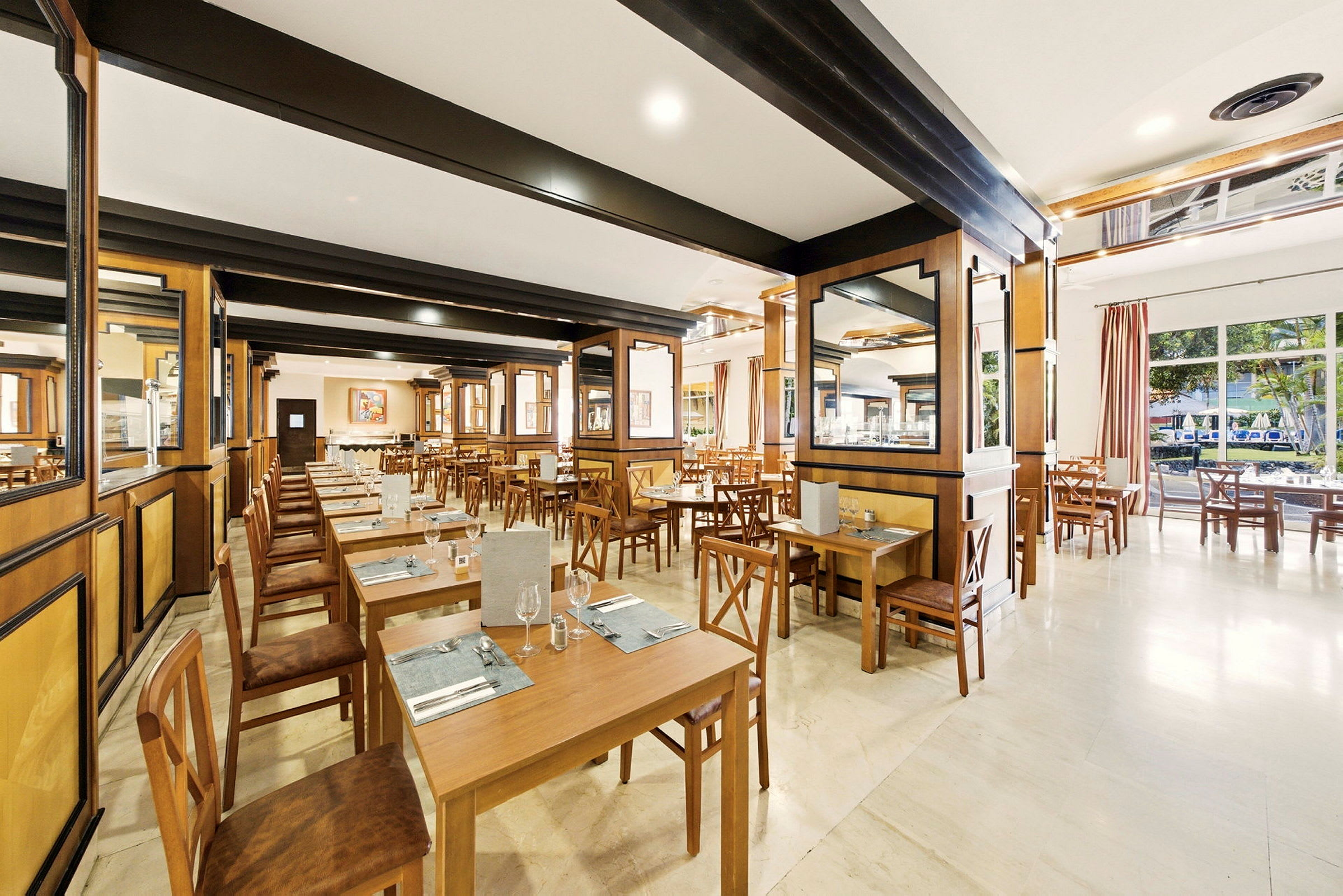 En rummelig restaurant med træborde og stole, lyst interiør og vinduer med udsigt til træer. (AI-genereret tekst)