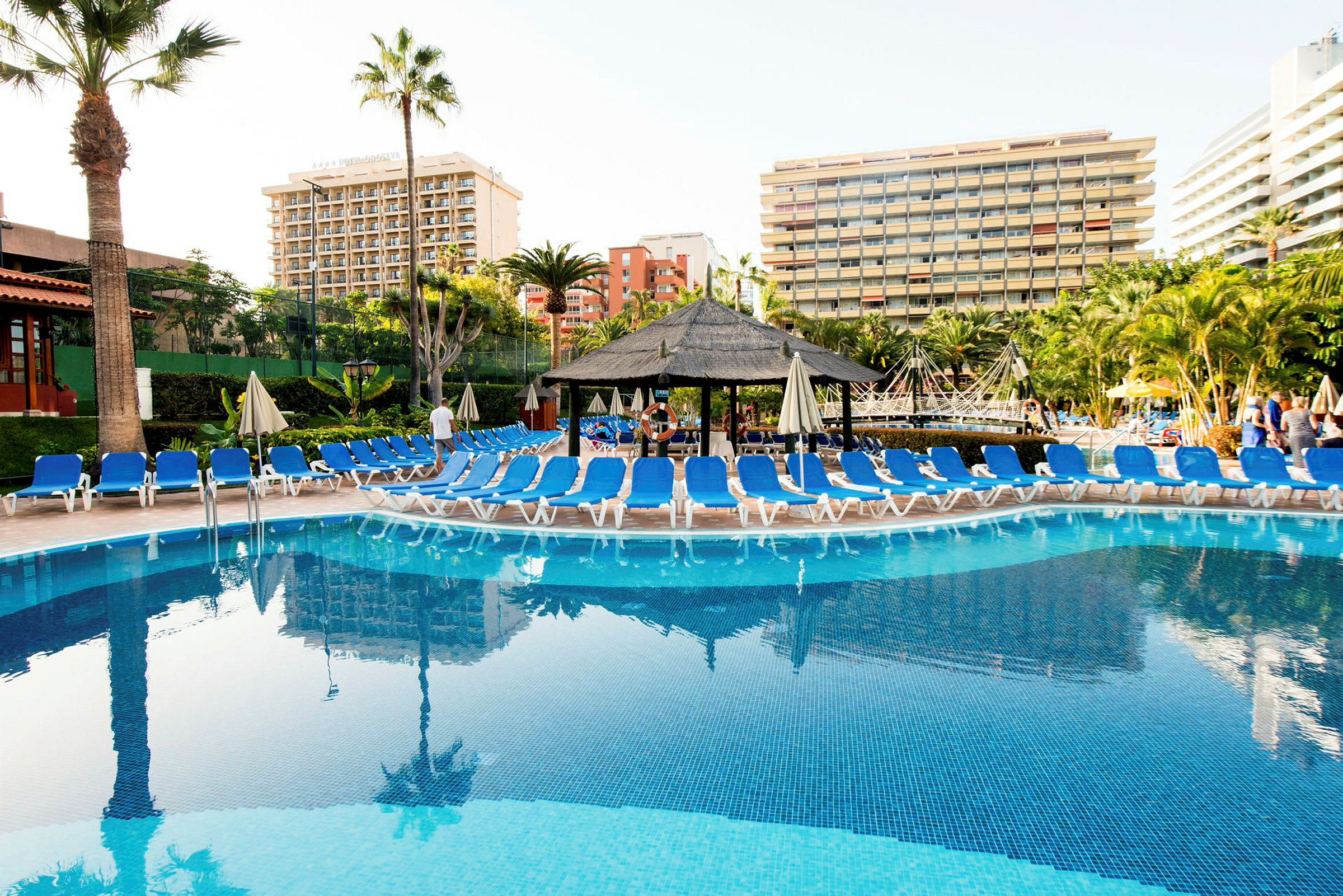 En pool med liggestole omkring og hotelbygninger i baggrunden. (AI-genereret tekst)
