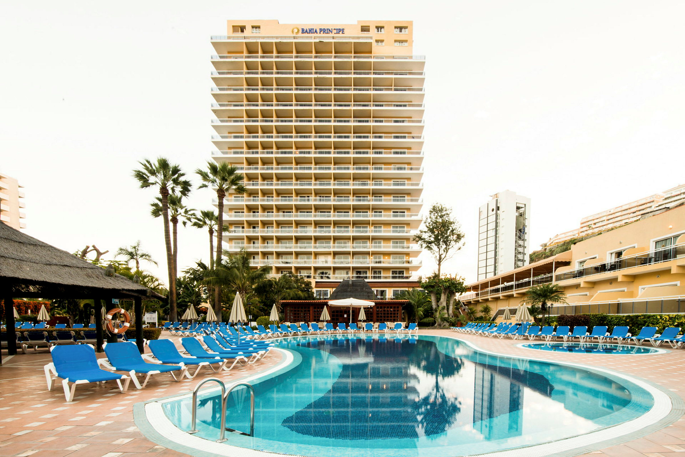 Hotelbygning med pool og liggestole foran. (AI-genereret tekst)