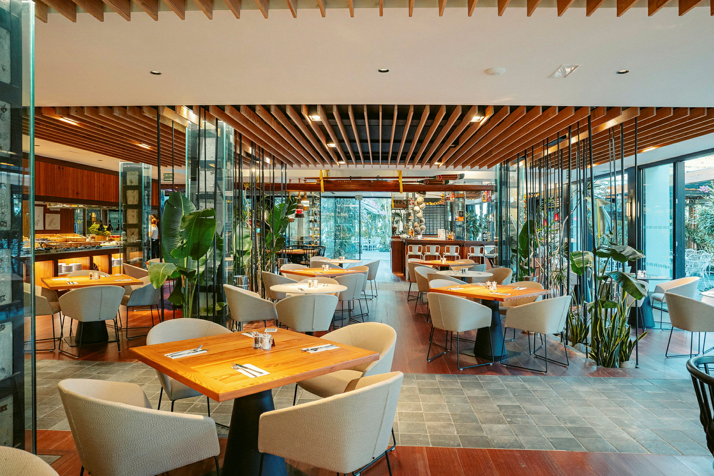 En moderne restaurantindretning med træborde, polstrede stole og store planteudsmykninger. (AI-genereret tekst)