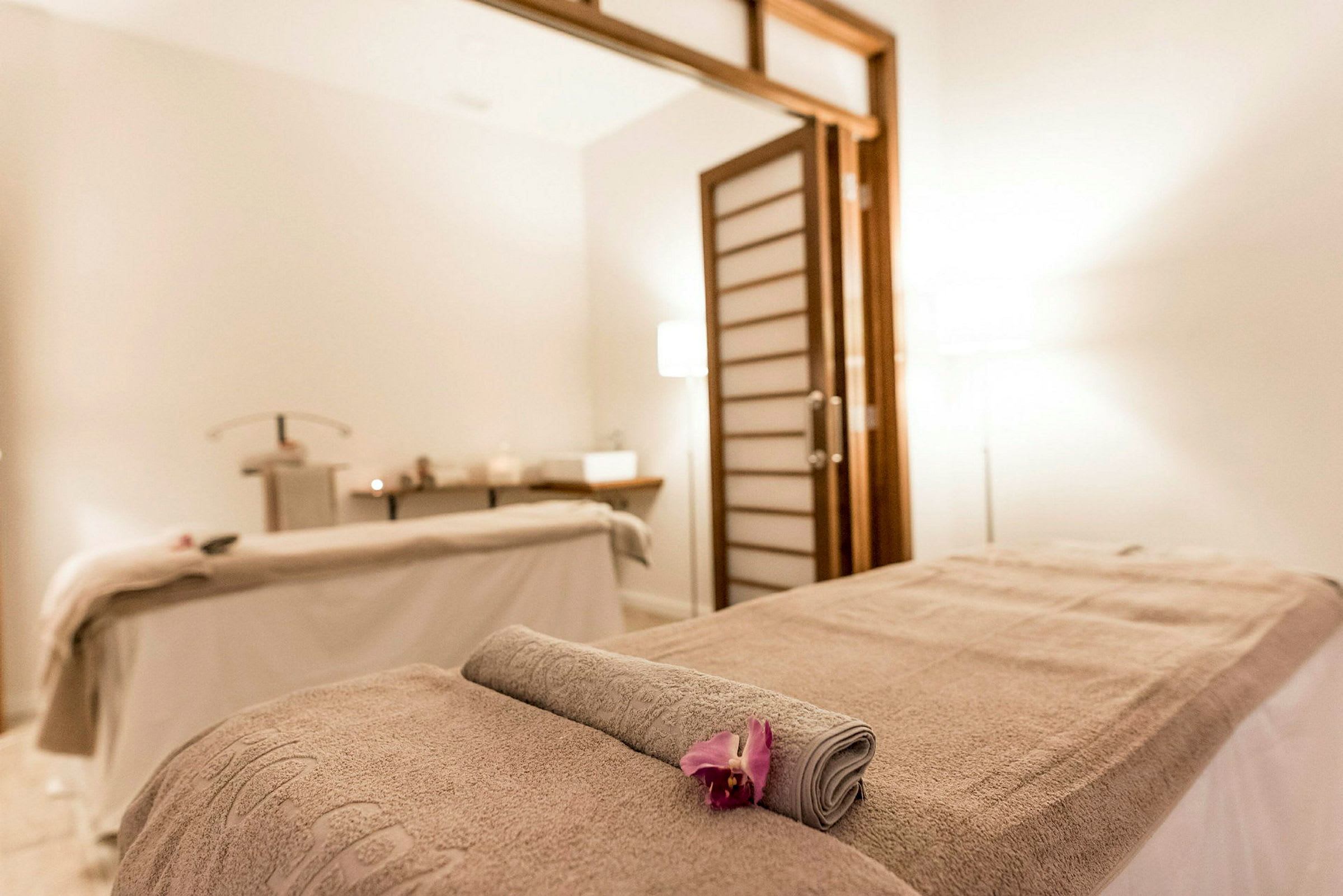 Et spa-behandlingsrum med massagebord, håndklæde og blomst. (AI-genereret tekst)