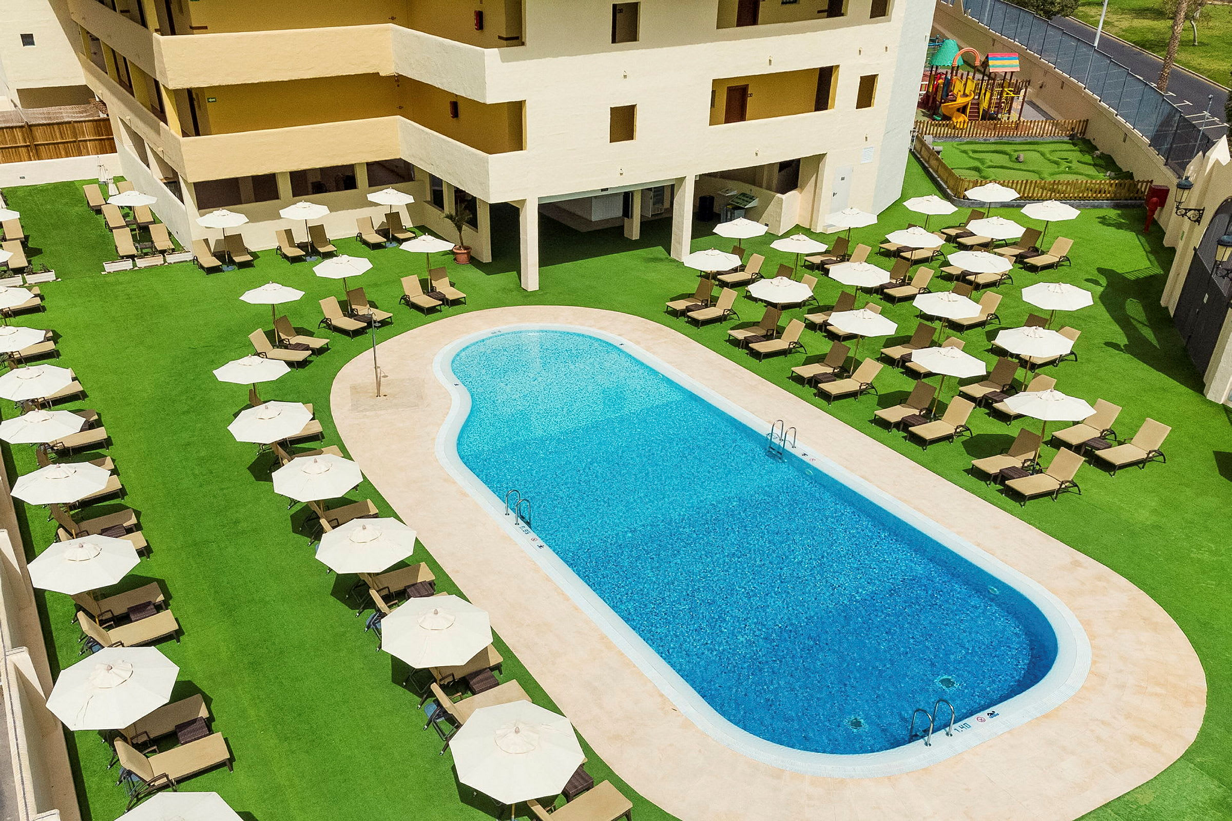 Billede der viser en udendørs pool omgivet af solsenge og parasoller ved et hotel. (AI-genereret tekst)