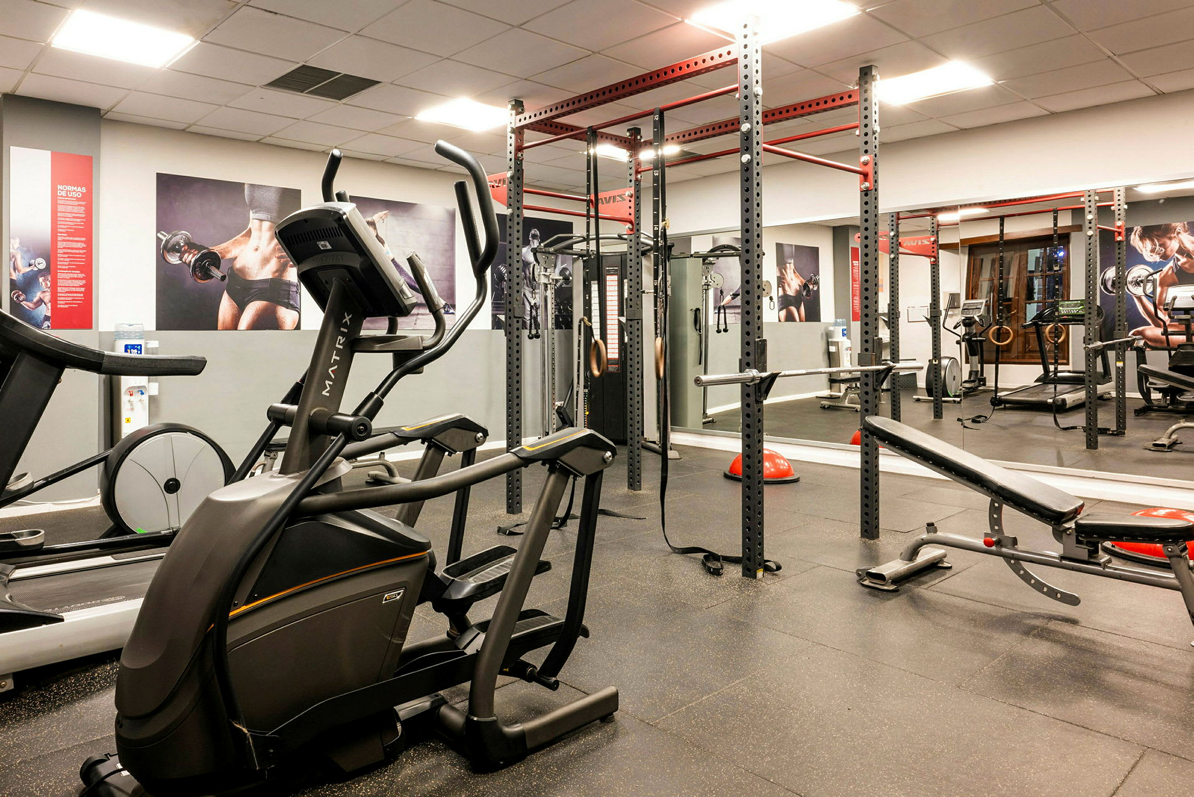 Billede af et fitnesscenter med træningsudstyr som løbebånd, træningsmaskiner og stativer. (AI-genereret tekst)