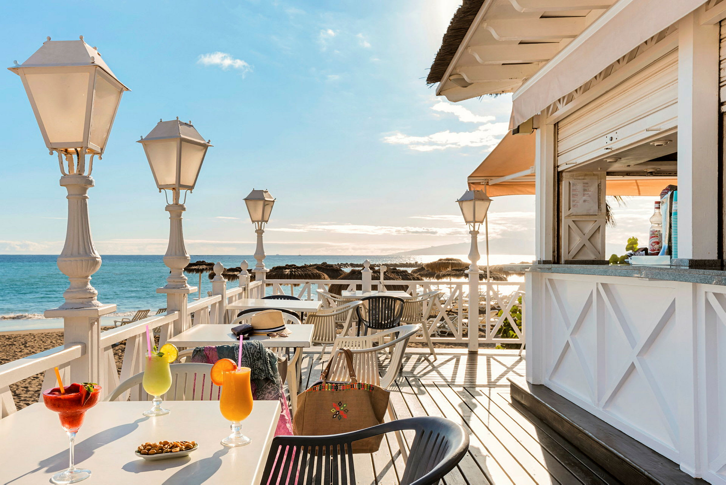 En strandcafé med borde, drikke og udsigt over havet. (AI-genereret tekst)