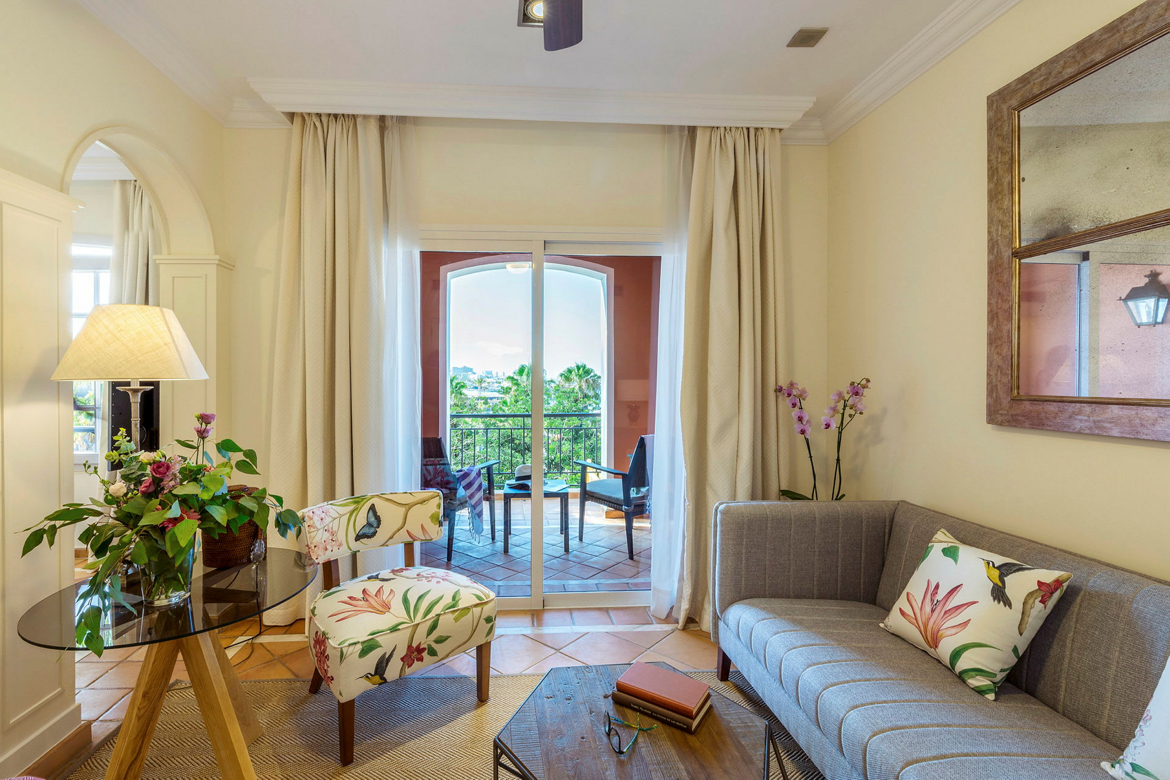 En stue med dekorativ stol, sofa og blomster, med udsigt til en balkon. (AI-genereret tekst)