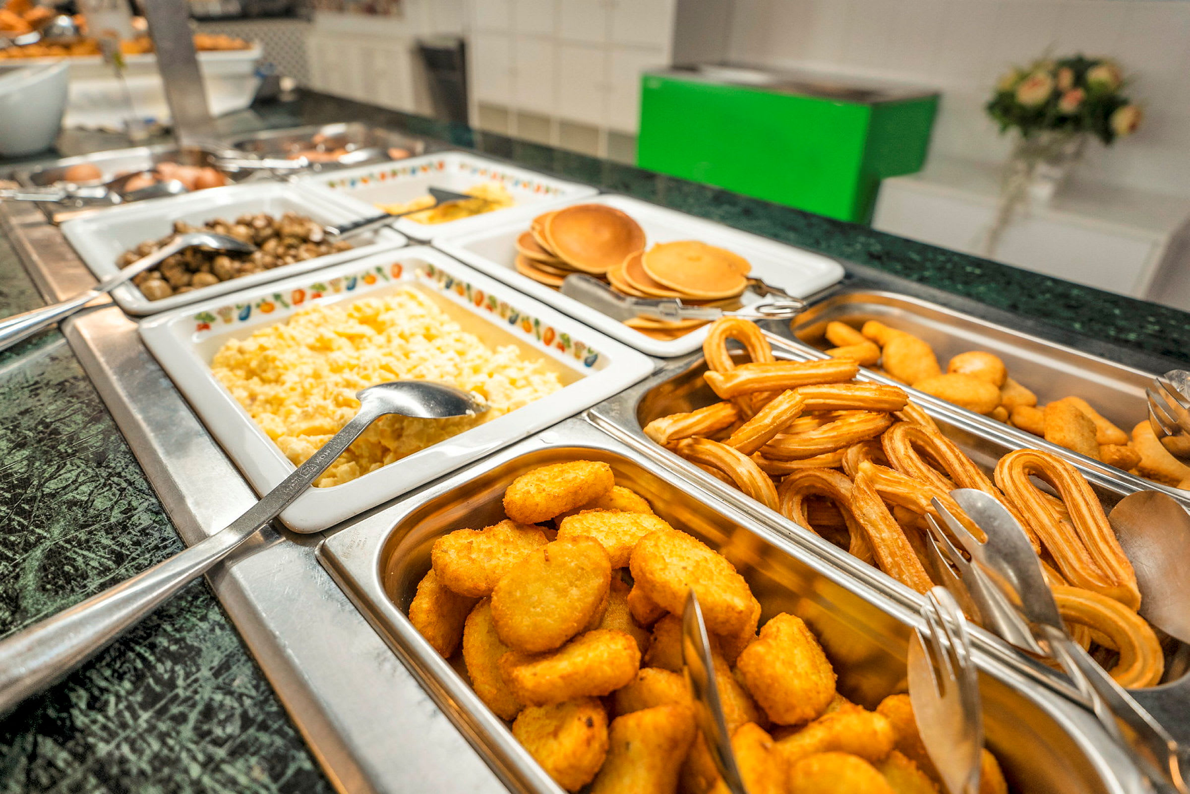 Billede af en buffet fyldt med forskellige retter, herunder røræg, pandekager, churros og sprøde nuggets. (AI-genereret tekst)