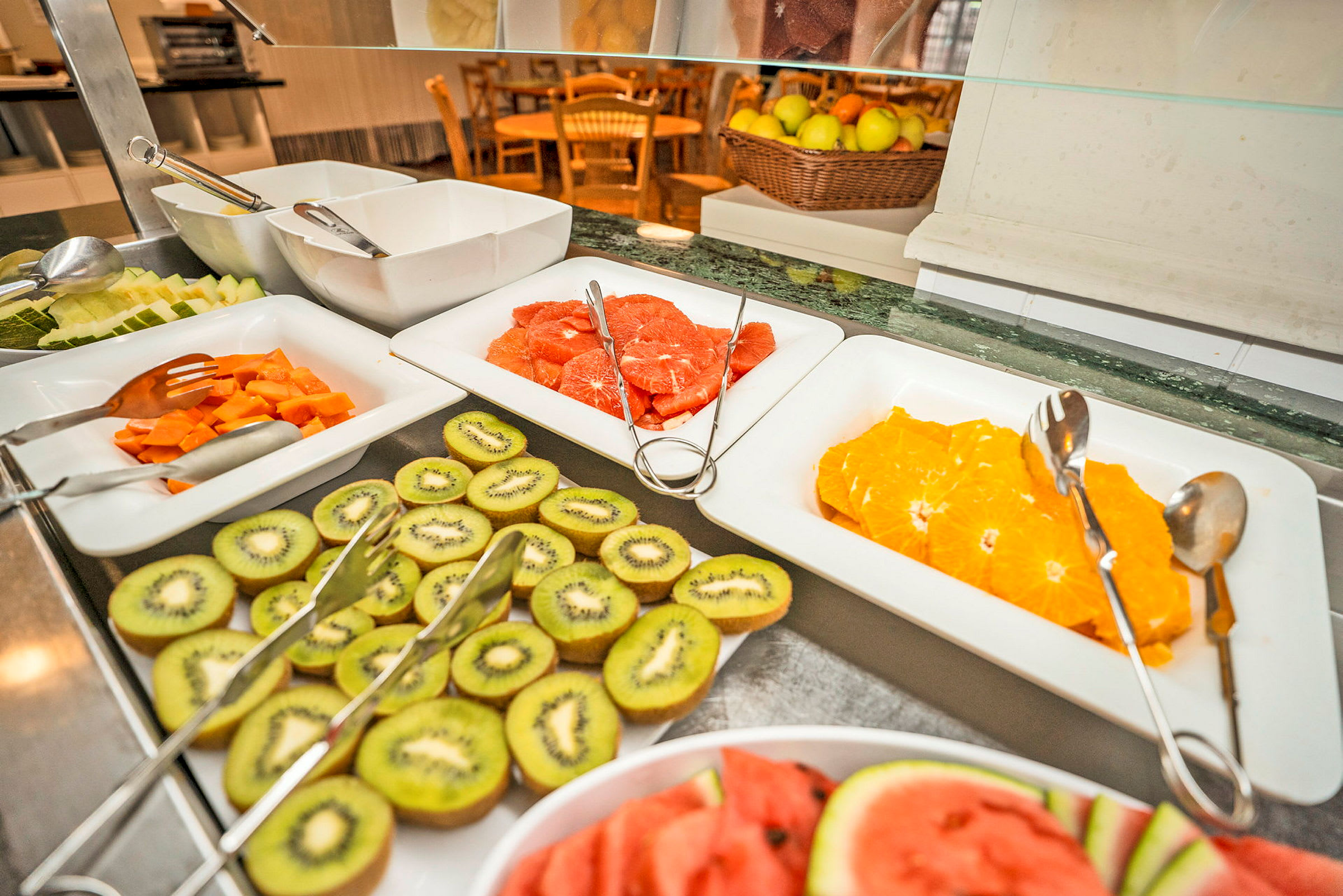 Buffetbord med skåret frugt som appelsiner, kiwi og vandmelon i fade. (AI-genereret tekst)