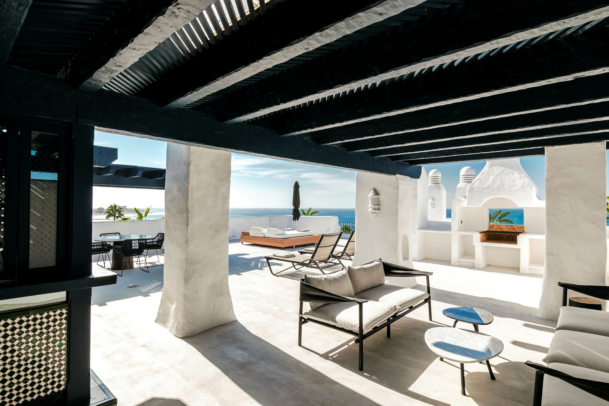 Solrig terrasse med hvide vægge, sorte træbjælker og moderne loungemøbler. (AI-genereret tekst)
