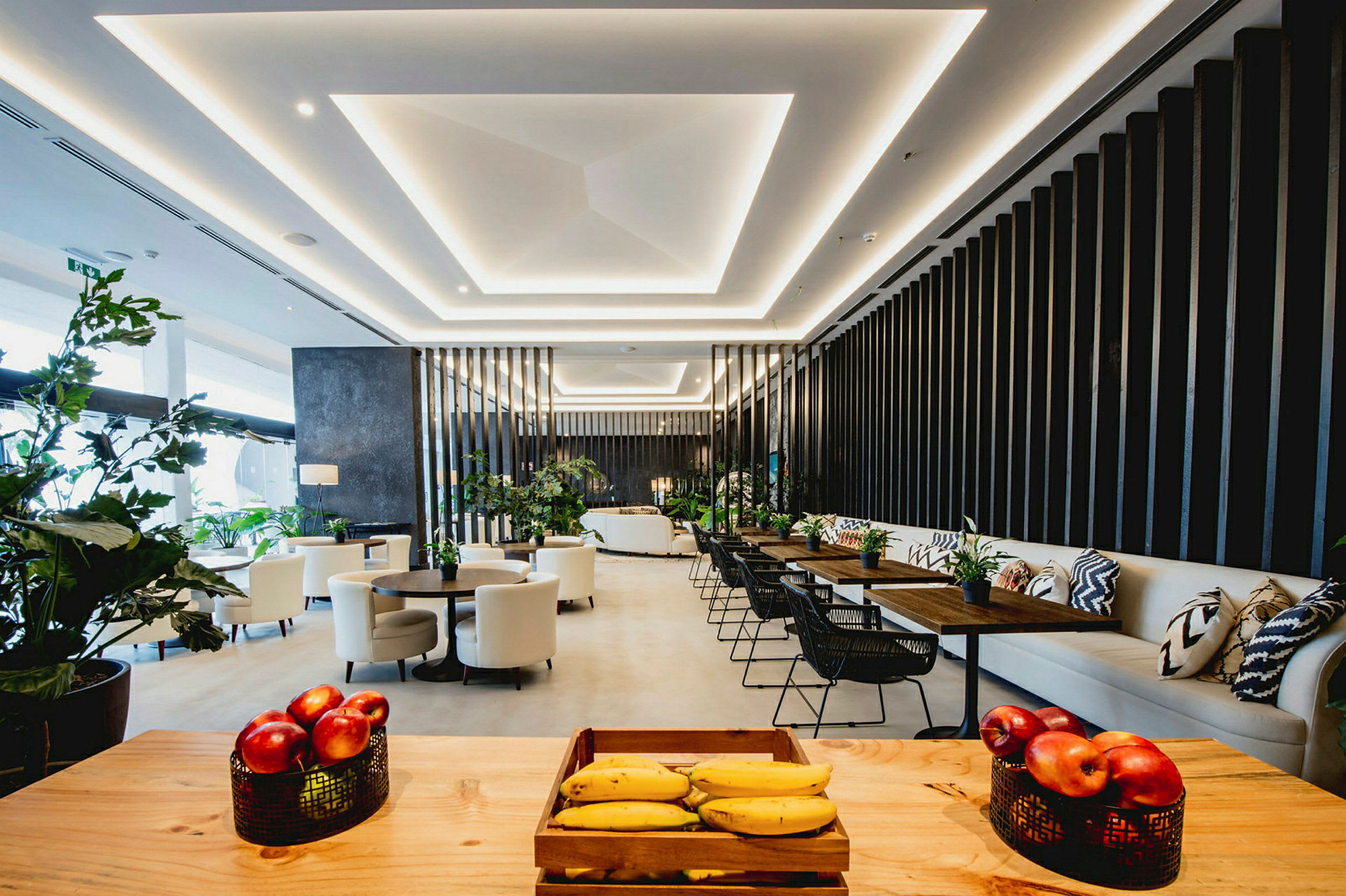 En moderne lounge med siddegrupper, dekorative planter og en frugtskål på et bord i forgrunden. (AI-genereret tekst)