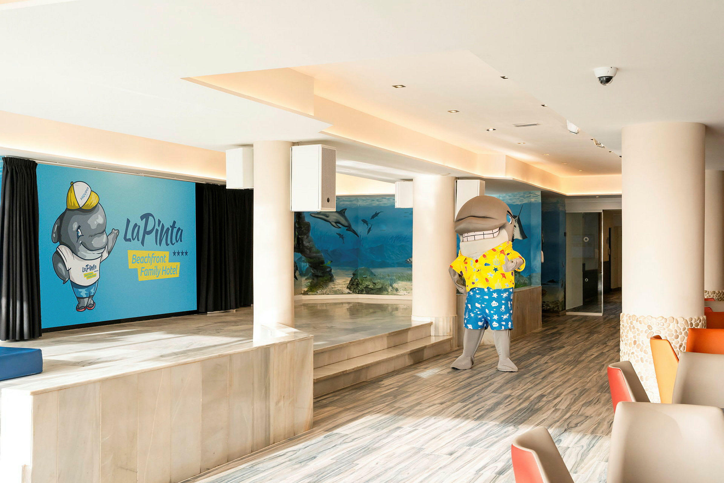 En hotelinteriør med en akvarievæg og en delfinmaskot. (AI-genereret tekst)