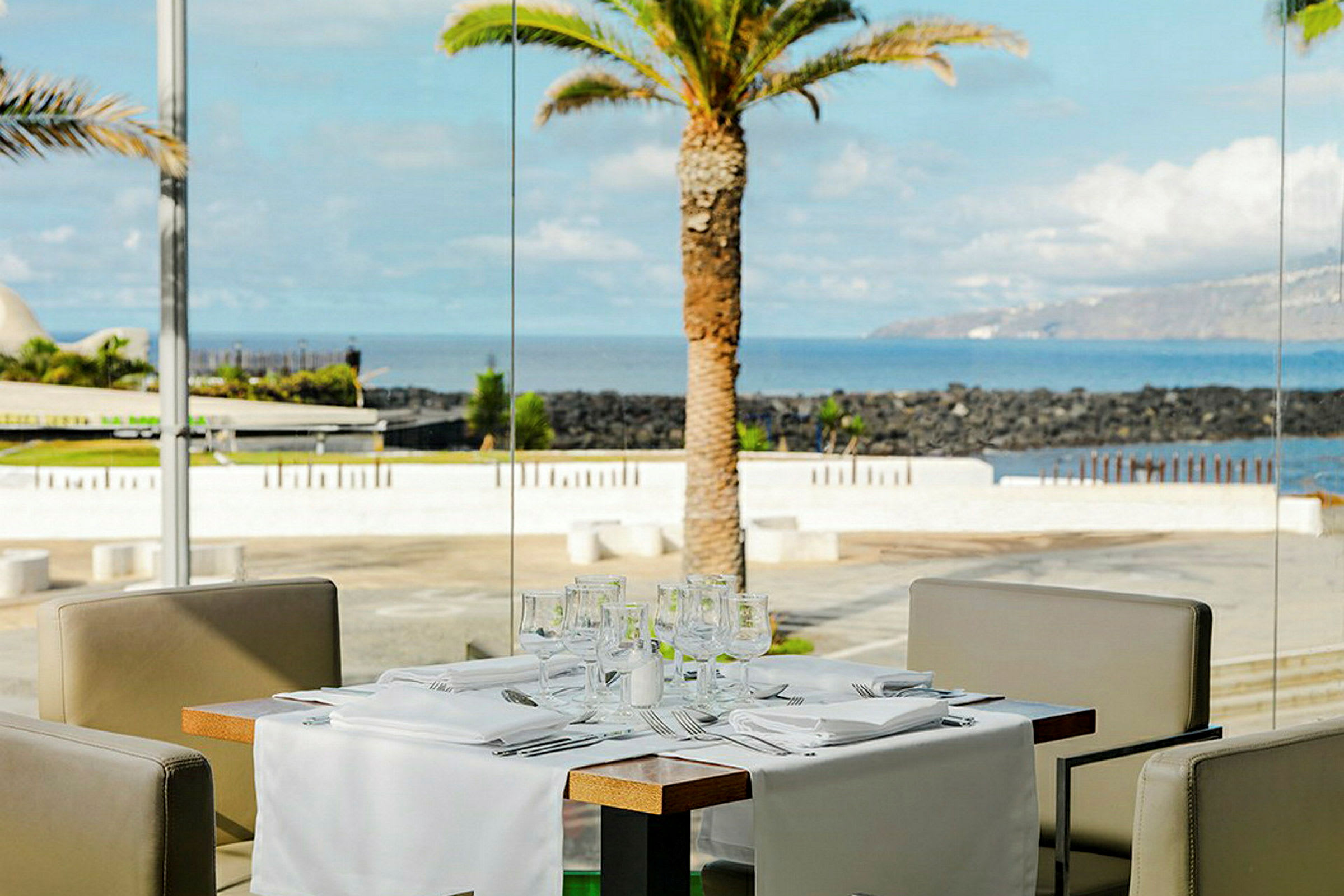 Et dækket udendørs bord i en restaurantmiljø med havudsigt og en palme i baggrunden. (AI-genereret tekst)