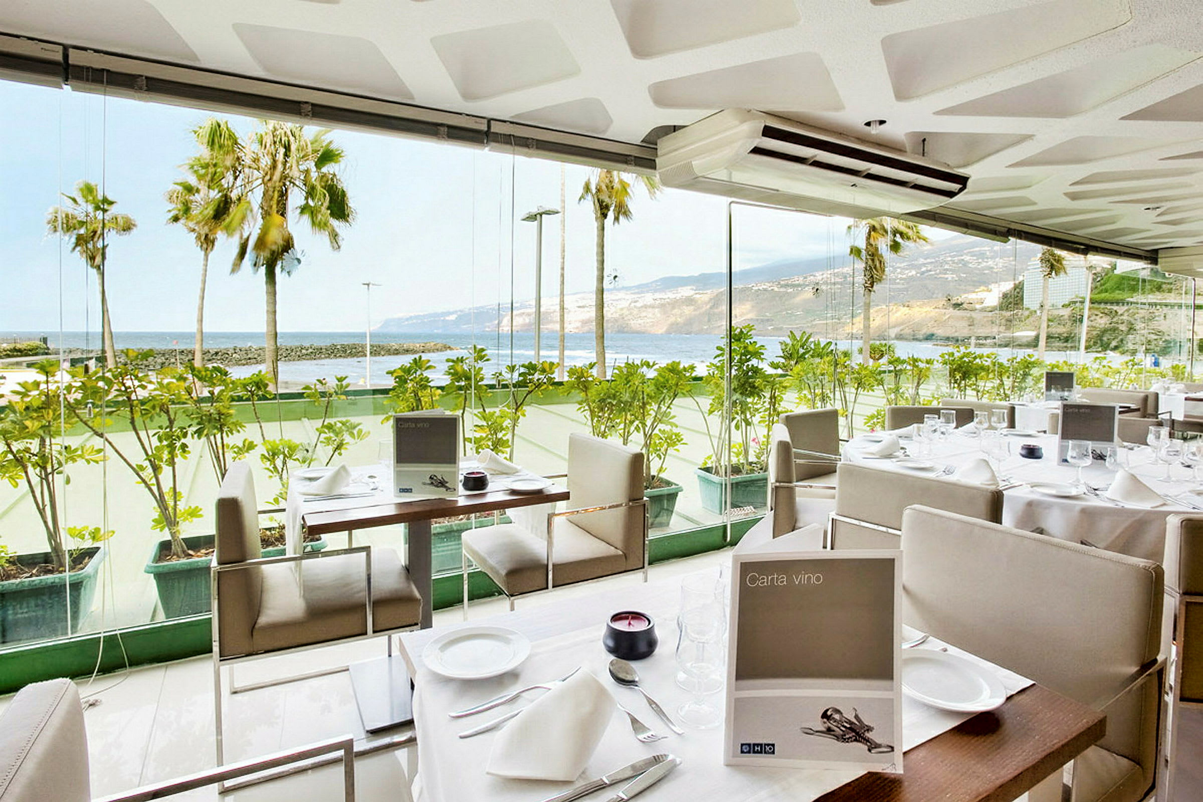 En restaurant med glasvægge og udsigt over havet og palmer. (AI-genereret tekst)