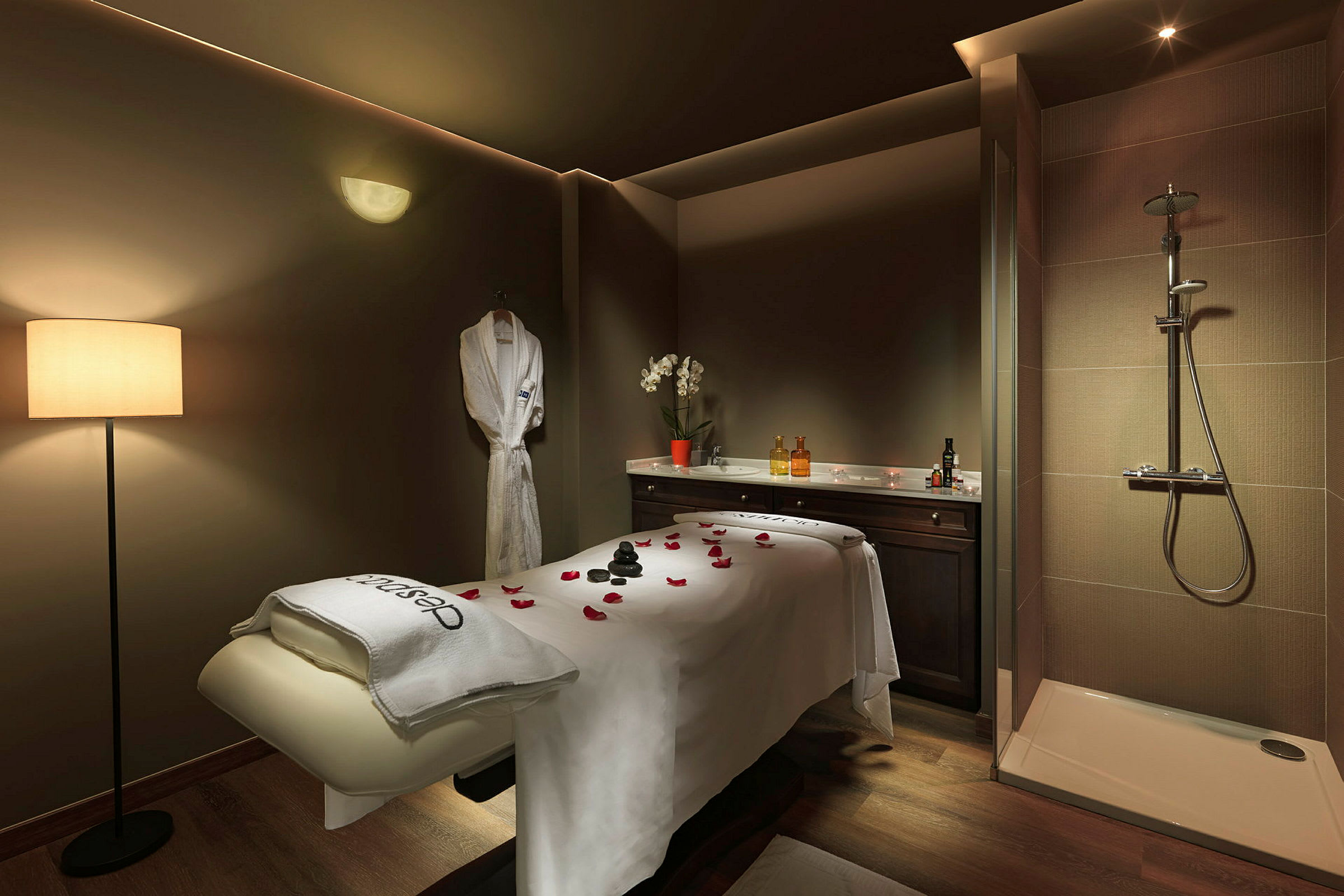 Et spa- eller massagebehandlingsrum med en behandlingsbænk, en bruser og en badekåbe hængende på væggen. (AI-genereret tekst)
