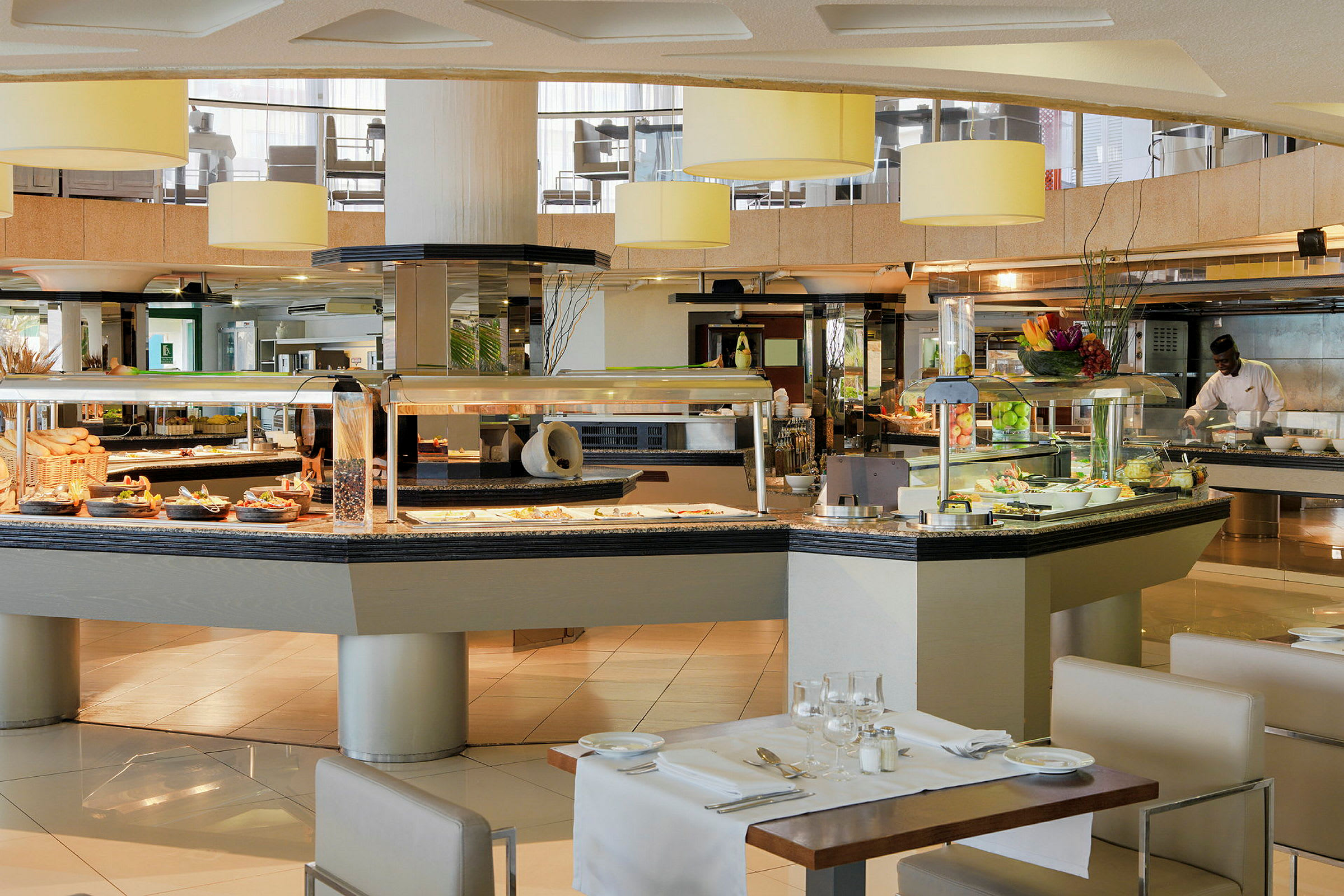 Buffetområde med borde dækket op til måltider. Flere retter og frugt er placeret på buffetbordet. (AI-genereret tekst)