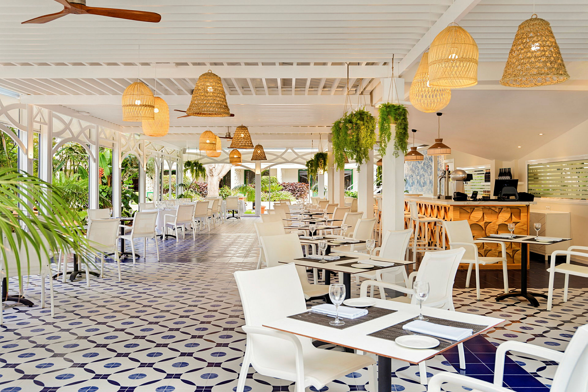 Billede af en restaurant med hvide møbler, dekorativt flisebelagt gulv og loftslamper i flet. Grønne planter hænger fra loftet. (AI-genereret tekst)