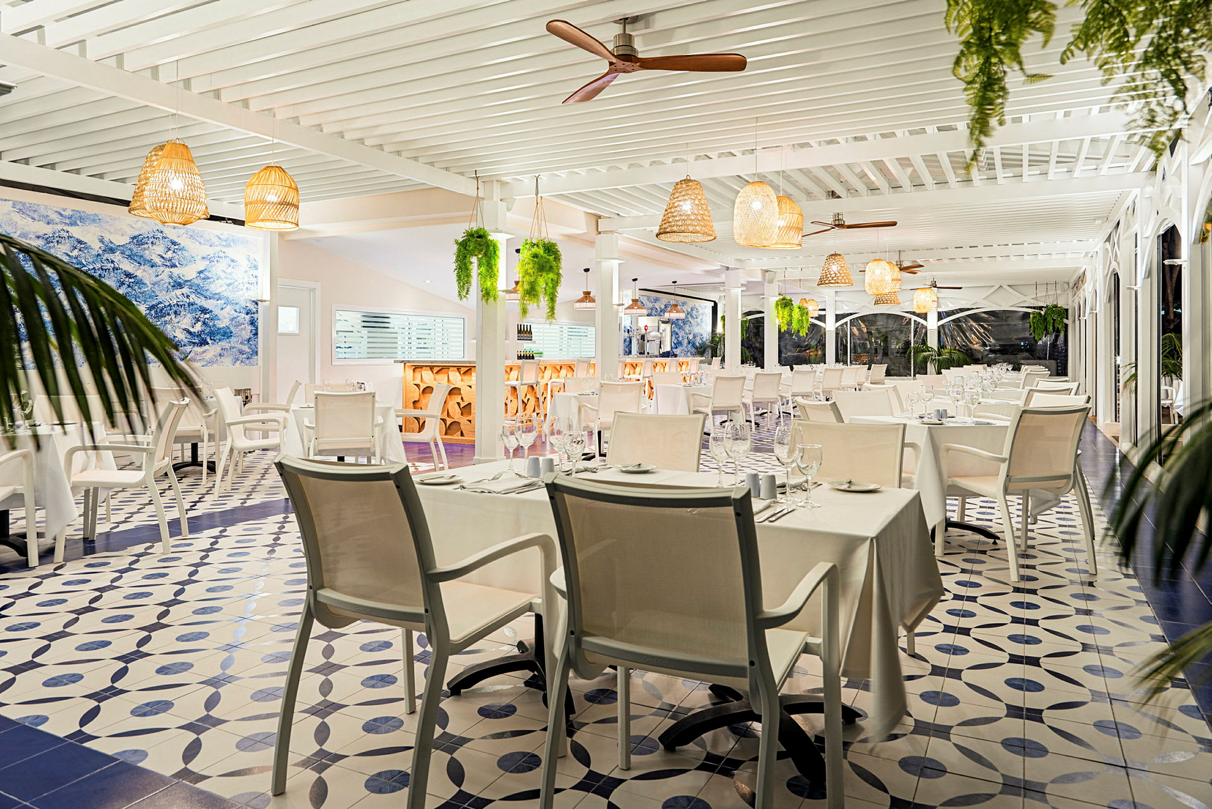 En lys restaurant med hvide duge og moderne møbler. Loftslamper og planter hænger fra loftet. (AI-genereret tekst)
