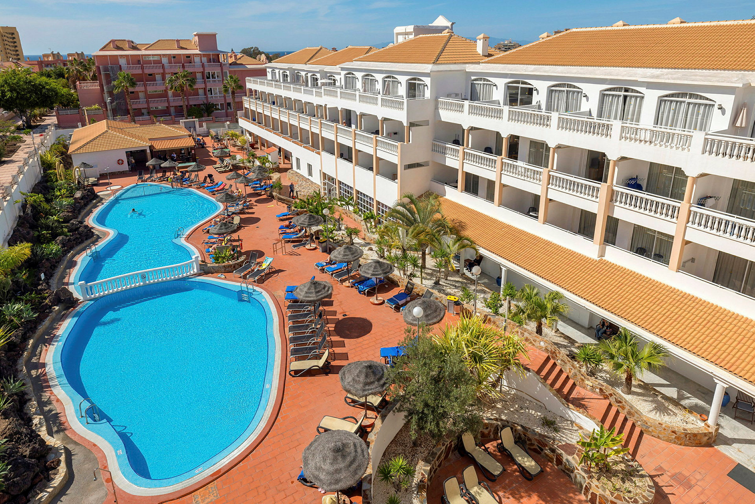 Udendørs udsigt over et hotel med solterrasse og pool. (AI-genereret tekst)