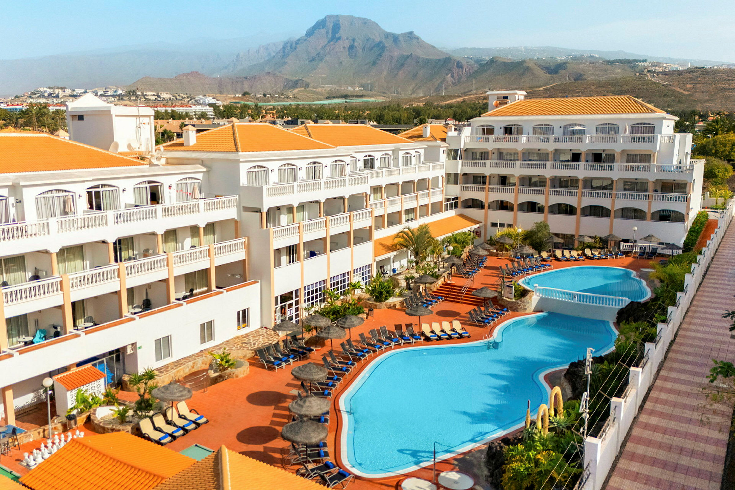 Hotel med poolområde og bjerge i baggrunden. (AI-genereret tekst)