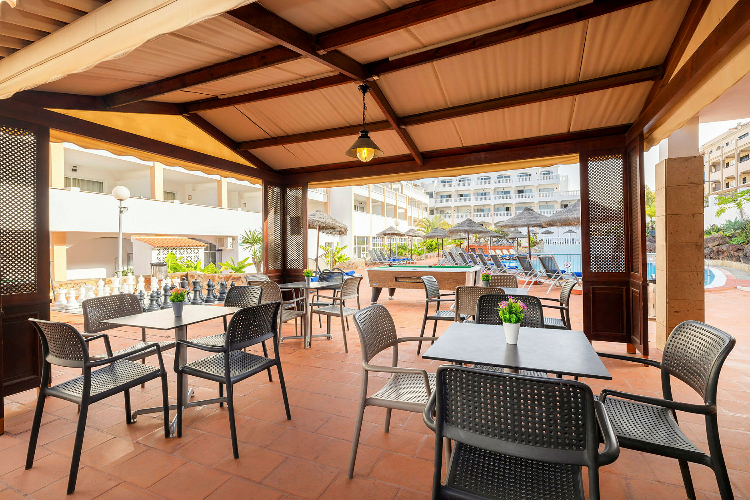Billede af en åben terrasse med borde og stole foran en udendørs pool. (AI-genereret tekst)