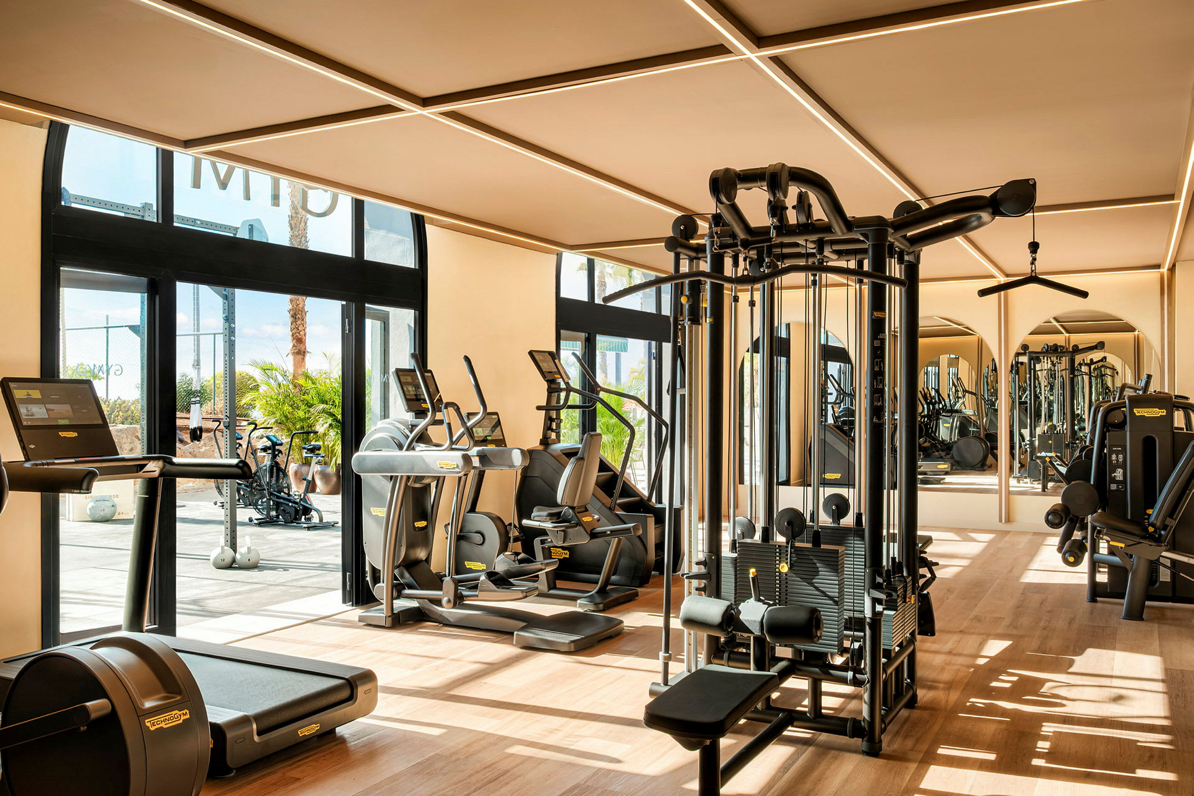 Billede af et fitnesscenter med forskellige træningsmaskiner og vinduer, der lukker dagslys ind. (AI-genereret tekst)
