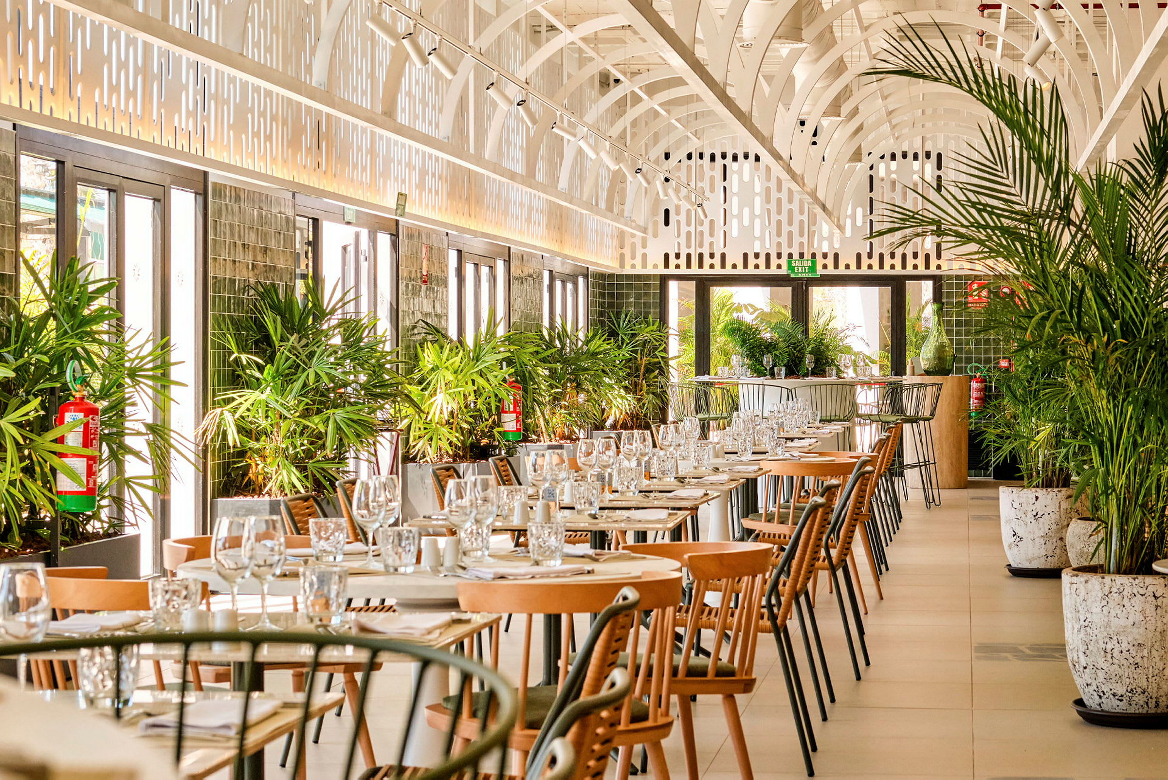 En restaurant med opstillede borde og stole, dekoreret med grønne planter. (AI-genereret tekst)
