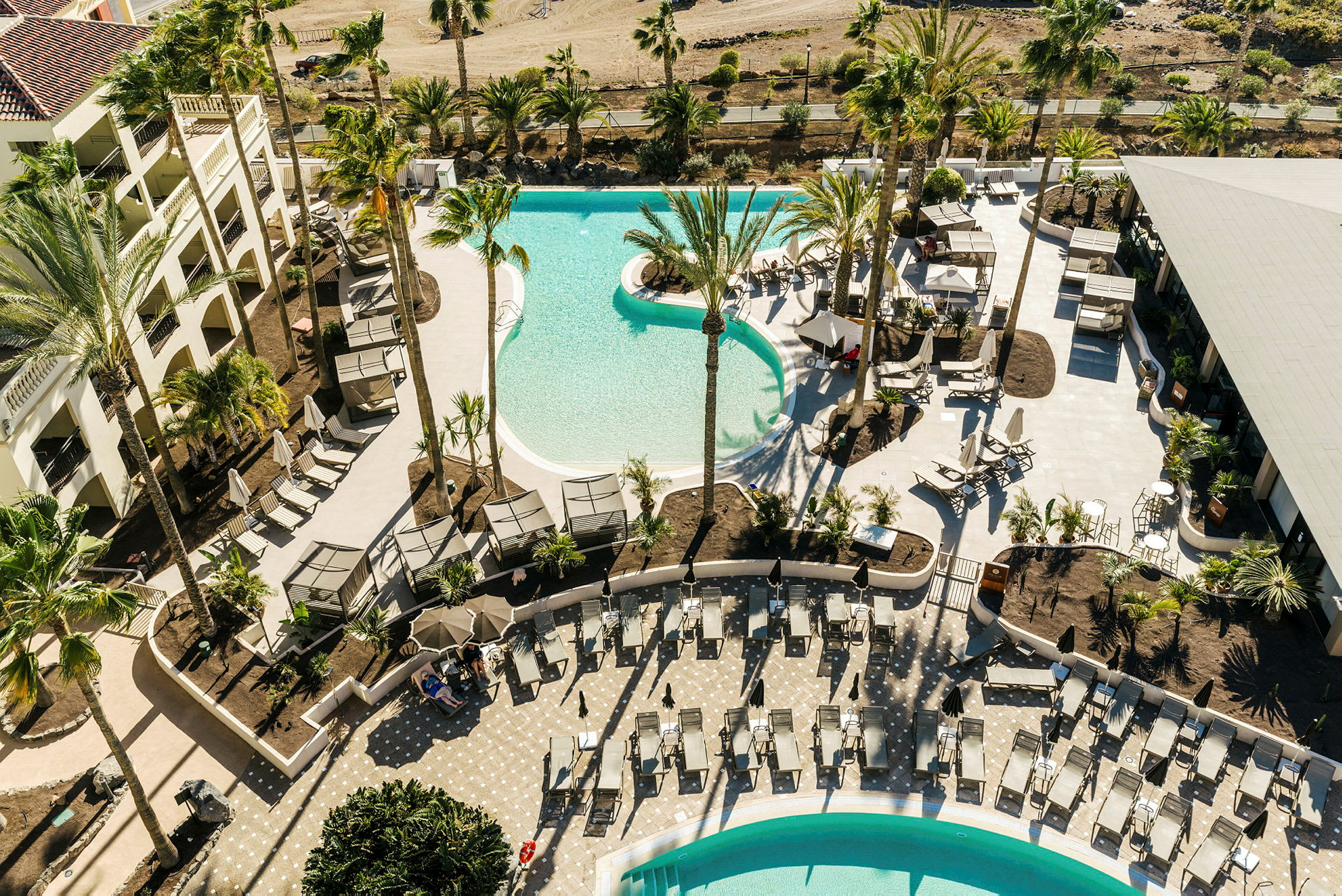 Luftfoto af et hotelområde med pools og liggestole omgivet af palmer. (AI-genereret tekst)