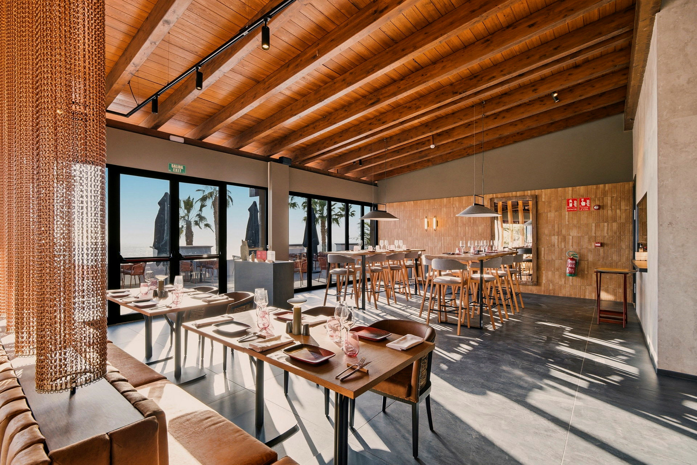 Interiør af en moderne restaurant med træmøbler og dækkede borde, store vinduer med udsigt ud. (AI-genereret tekst)