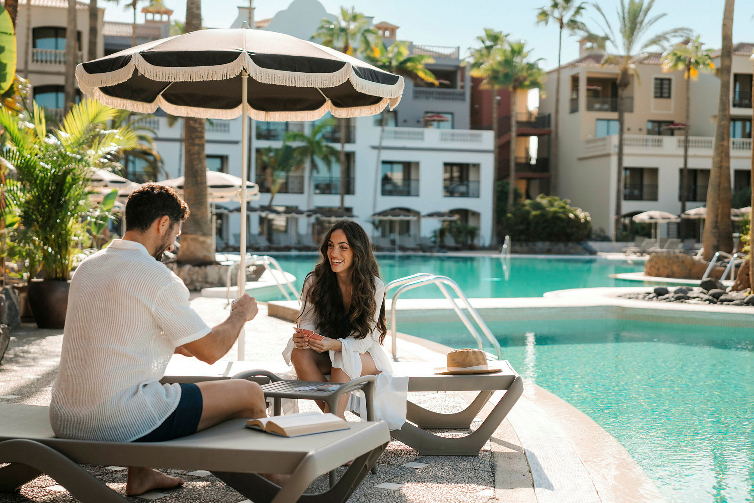 Personer sidder ved en pool under en parasol. (AI-genereret tekst)