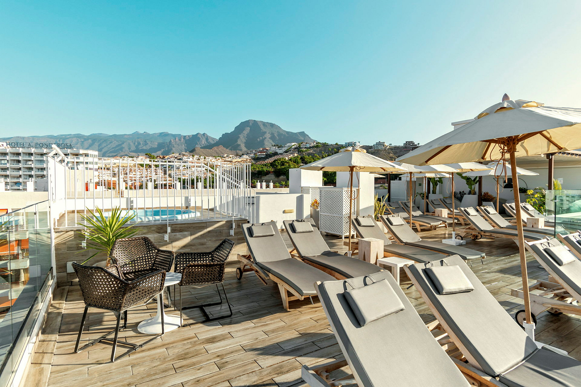Pool med liggestole og parasoller på en hotelterrasse med bjerge i baggrunden. (AI-genereret tekst)