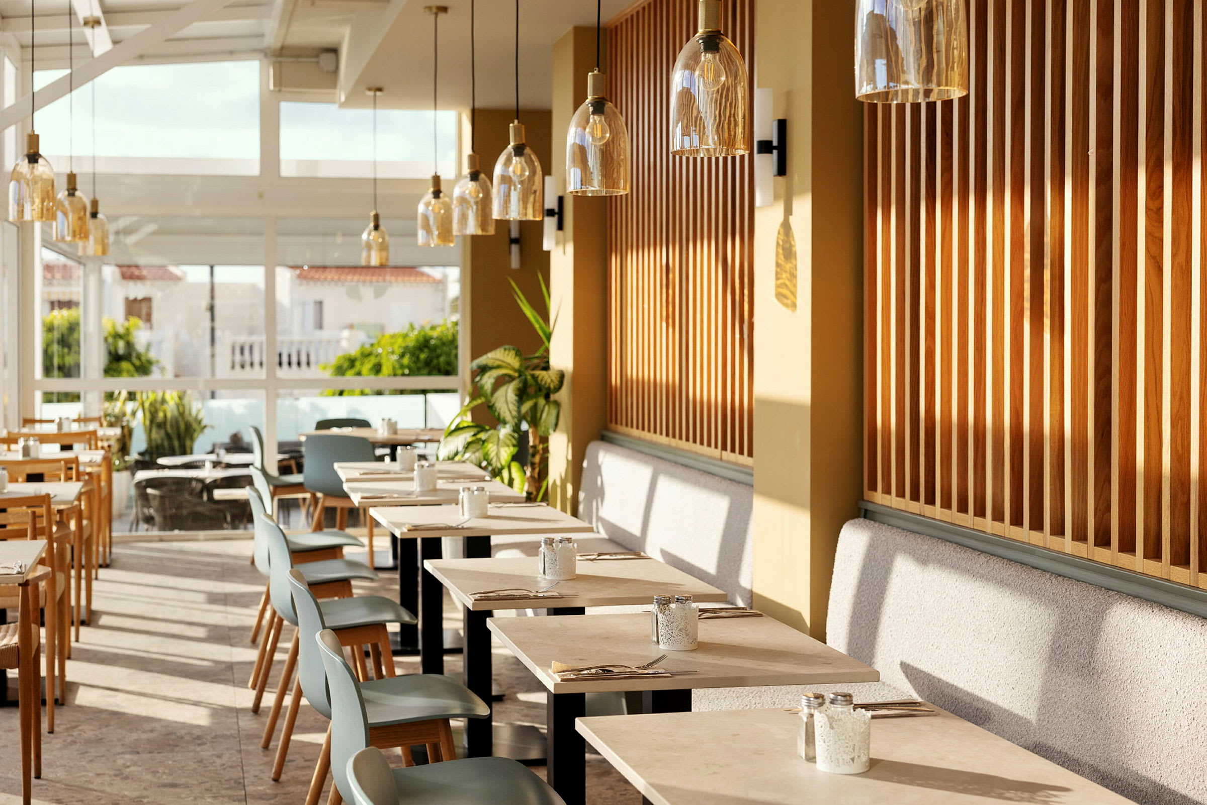 En restaurantinteriør med moderne borde og stole, omgivet af store vinduer og planter. (AI-genereret tekst)