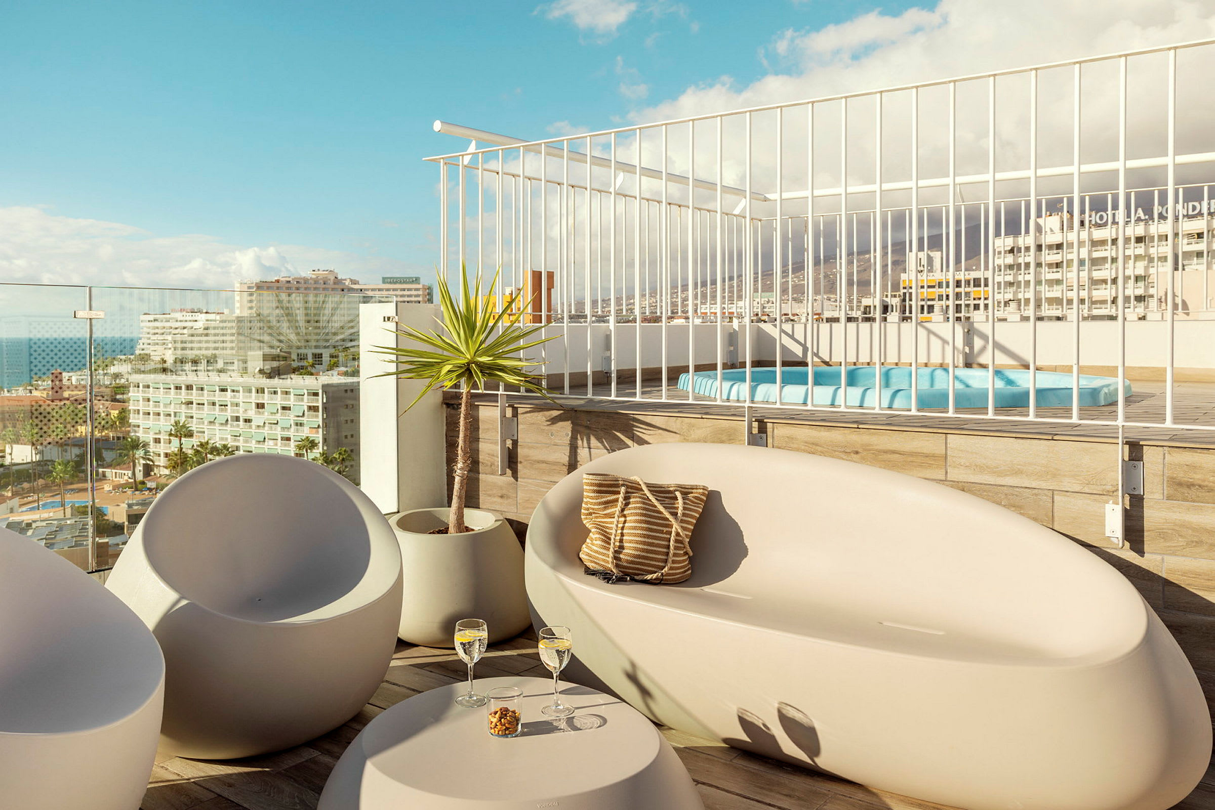 Udsigt over en møbleret terrasse med siddepladser og jacuzzi samt byen i baggrunden. (AI-genereret tekst)