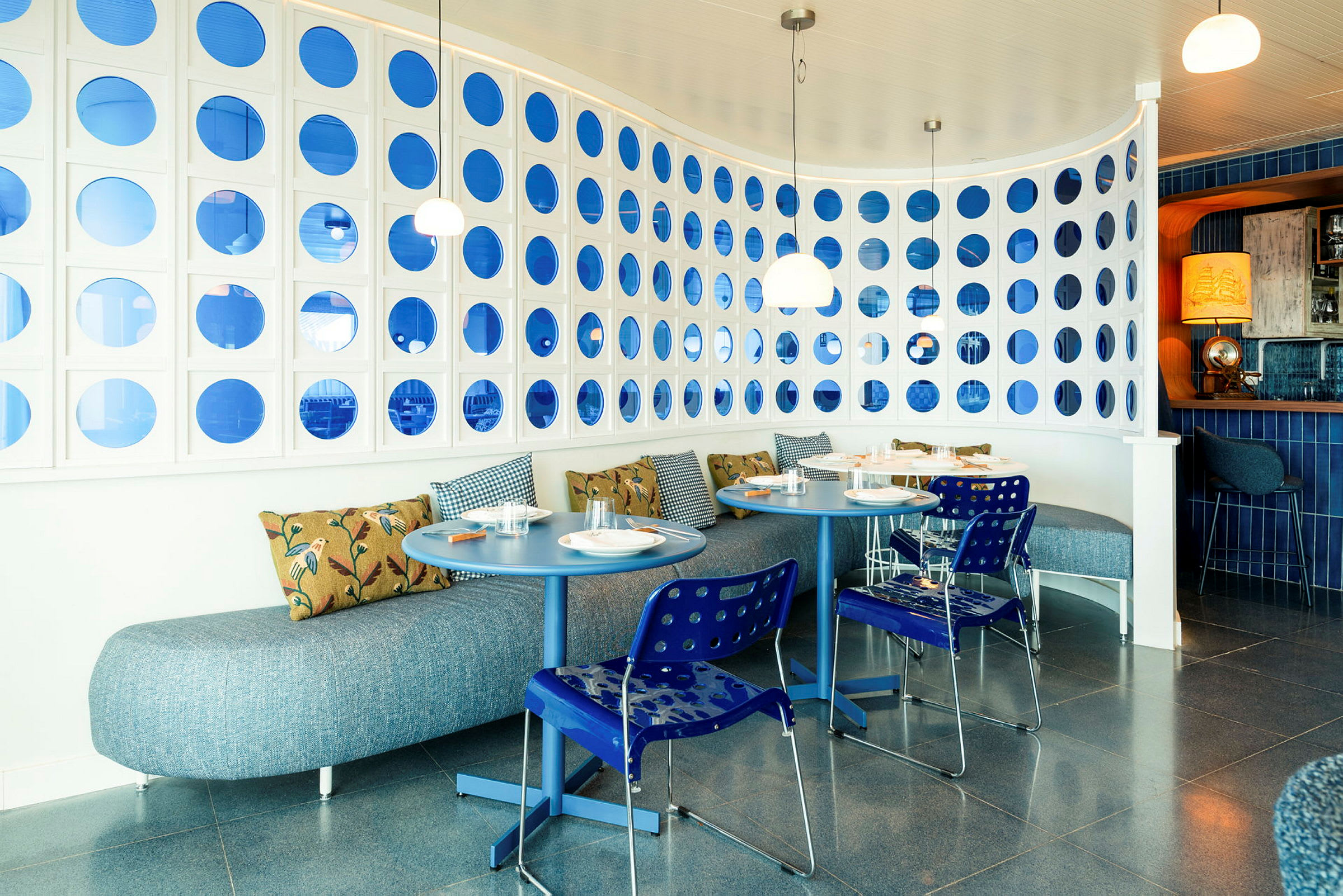 Et moderne restaurantområde med blå og hvide detaljer og runde borde. (AI-genereret tekst)