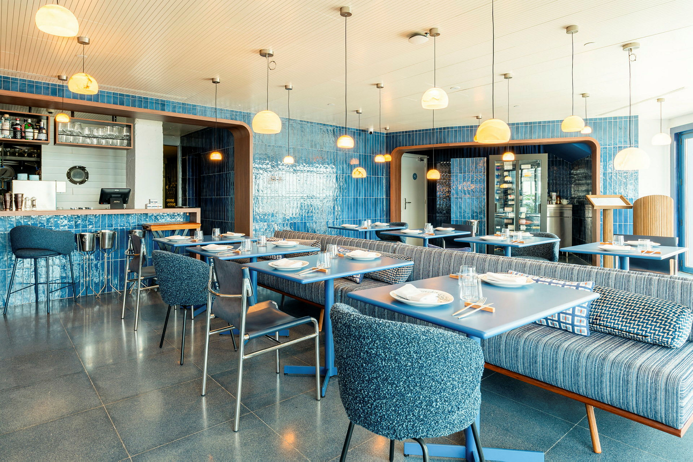 En farverig restaurantindretning med blå vægge, borde og stole. Lyse lamper hænger fra loftet. (AI-genereret tekst)