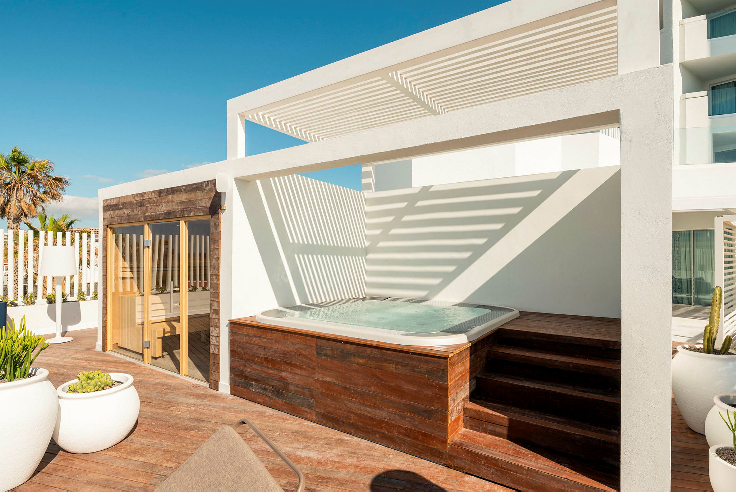En terrasse med et boblebad, en hvid pergola og en sauna med træbeklædt facade. (AI-genereret tekst)