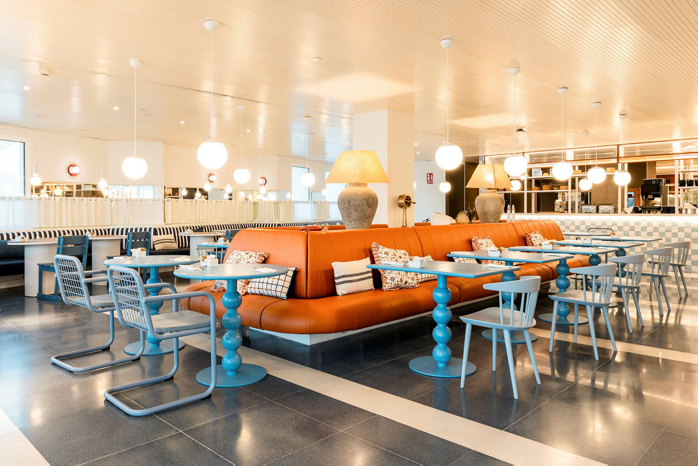 En moderne indrettet café med orange lædersofaer, blå borde og stole samt dekorative lamper i loftet. (AI-genereret tekst)