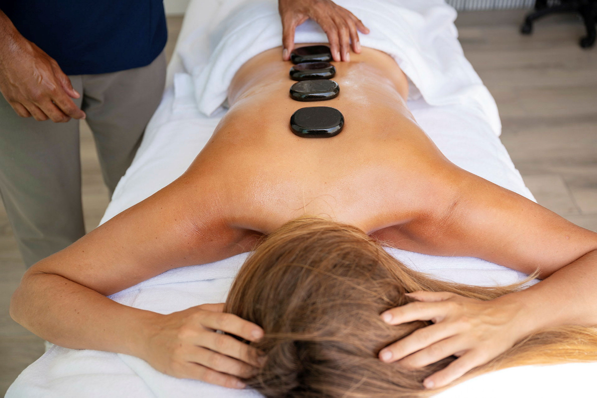 Massage udføres med varme sten, der er placeret på en kvindes ryg. (AI-genereret tekst)