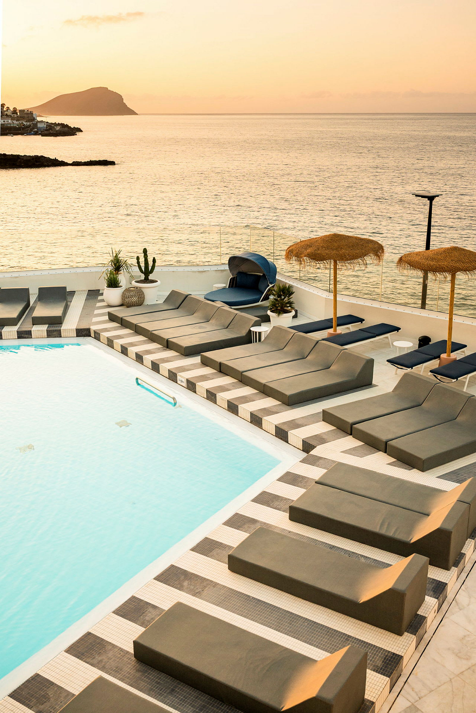 Poolområde med liggestole og udsigt over havet ved solnedgang. (AI-genereret tekst)