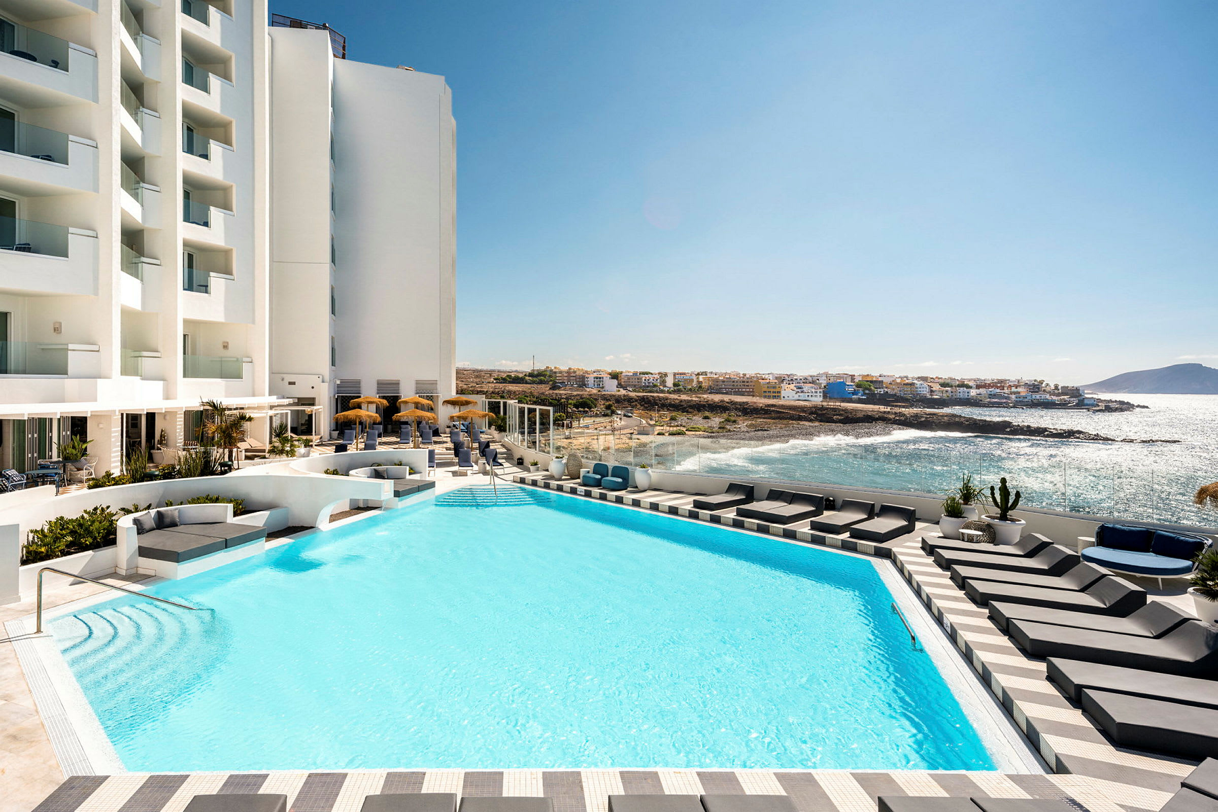 Hotellets poolområde med liggestole og udsigt over havet. (AI-genereret tekst)
