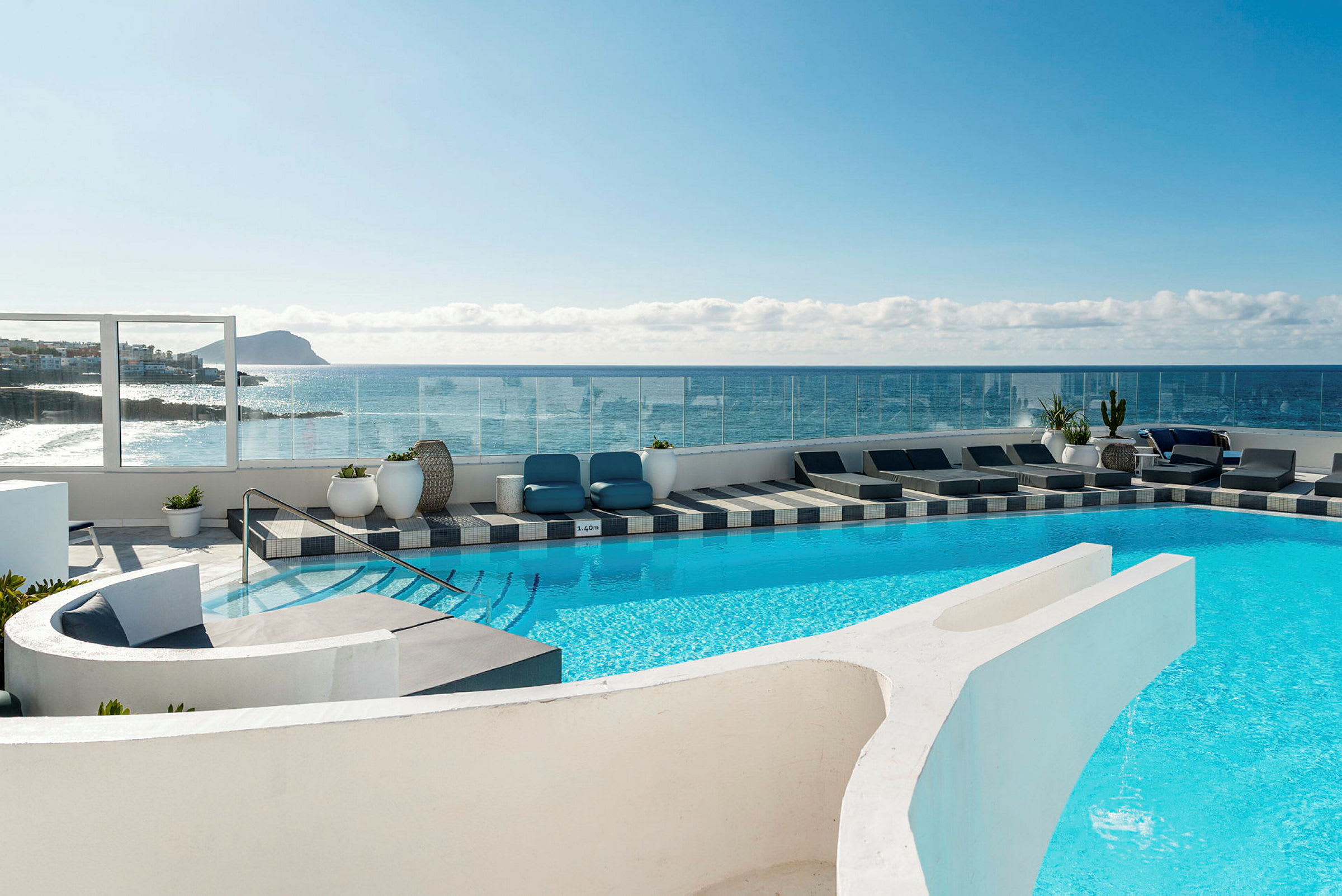 En udendørs pool ved et hotel med liggestole og udsigt over havet og en klippekyst. (AI-genereret tekst)