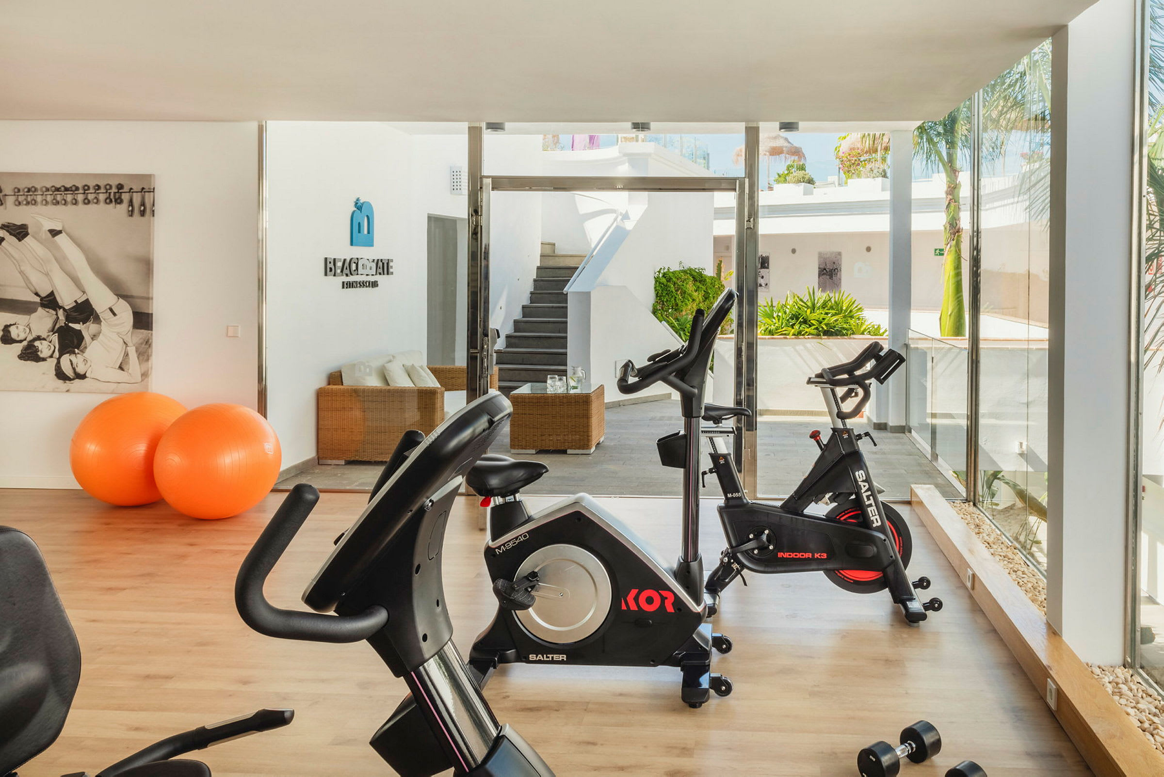 Et moderne fitnesscenter med motionscykler og orange balancebolde. Lys interiør og glasvægge. (AI-genereret tekst)
