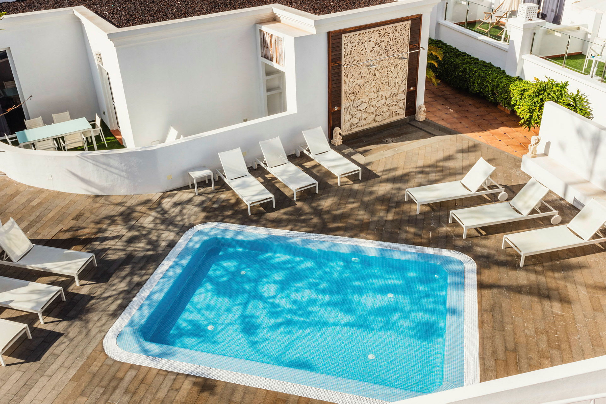 En lille swimmingpool med blåt vand omgivet af solsenge og et trægulv. (AI-genereret tekst)