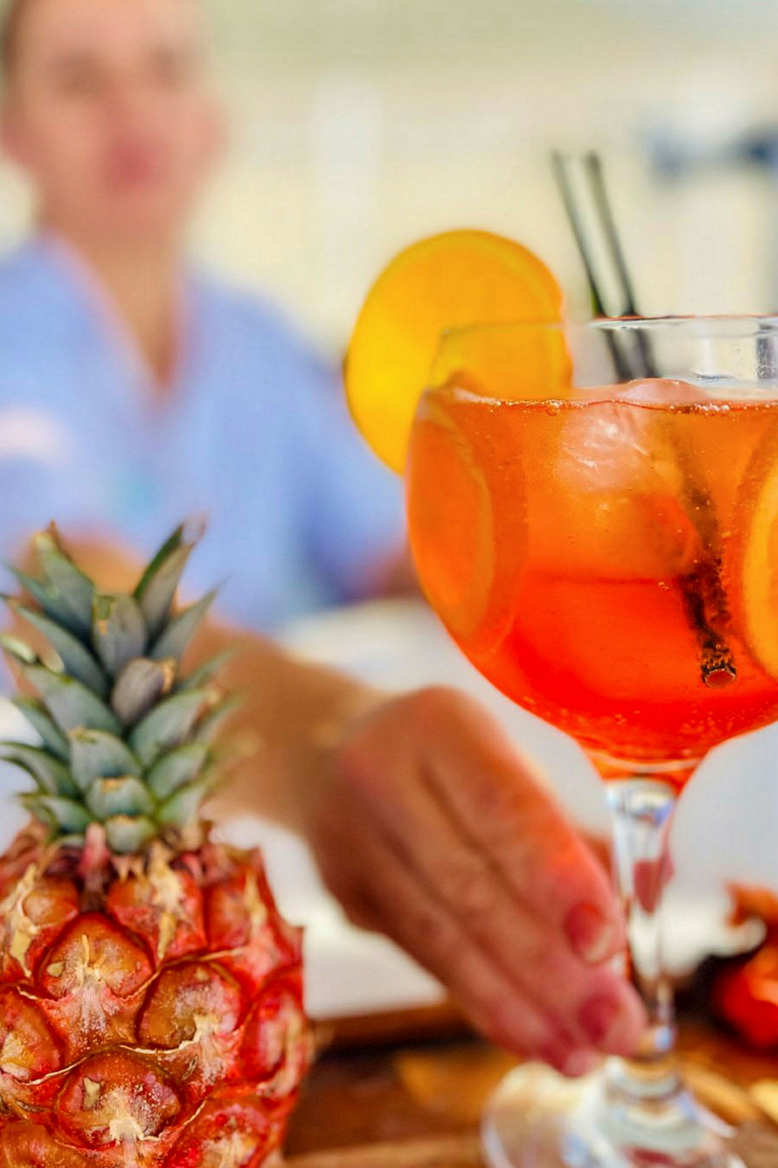 Et nærbillede af en drink i et glas med appelsinskiver og isterninger. En ananas ses i forgrunden. (AI-genereret tekst)
