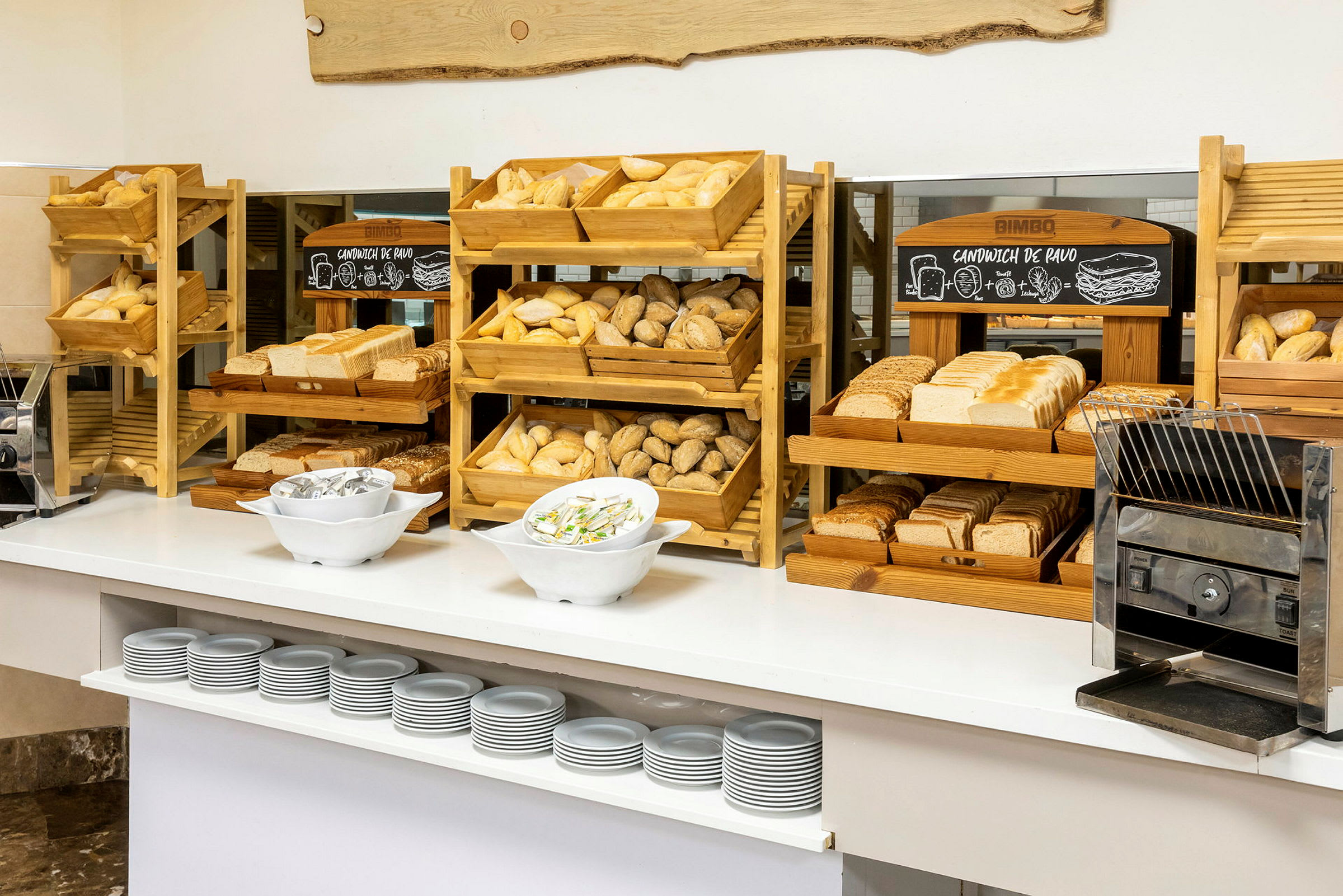 En morgenmadsbuffet med forskellige typer brød, skiveskåret og uskåret, på træstativer og en brødrister. (AI-genereret tekst)