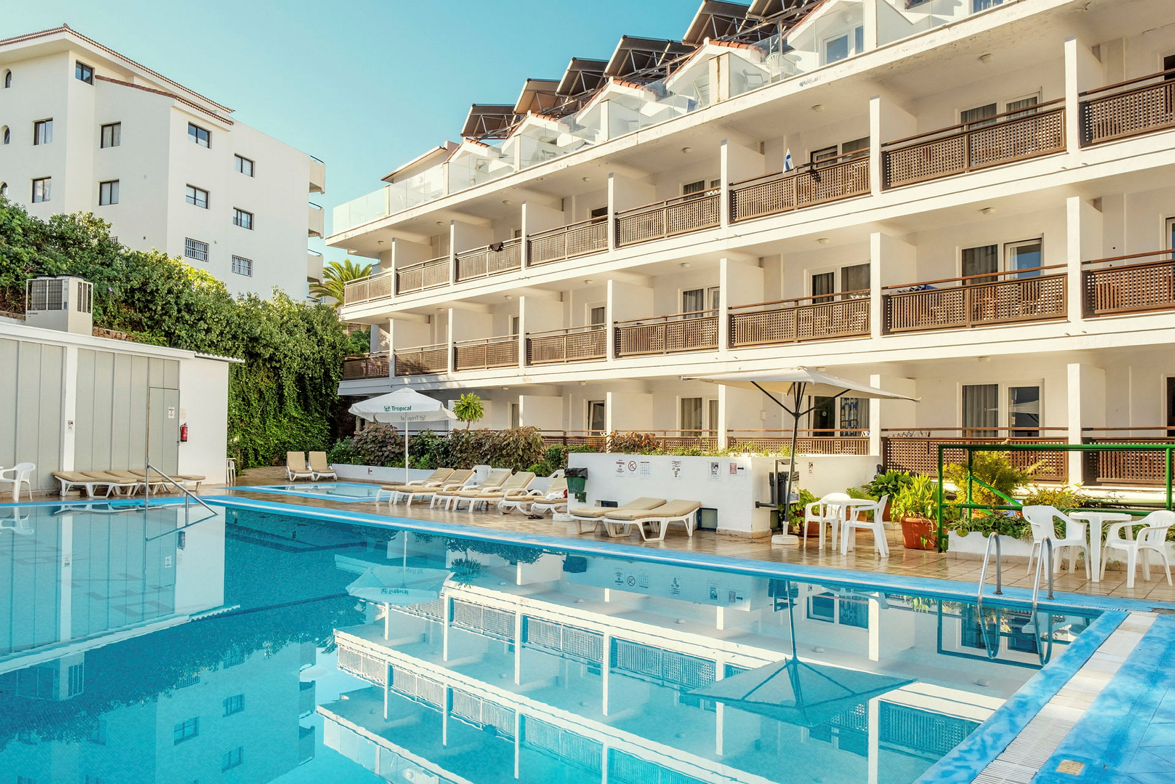 En hotelbygning med flere etager, ved siden af en udendørs pool og liggestole. (AI-genereret tekst)