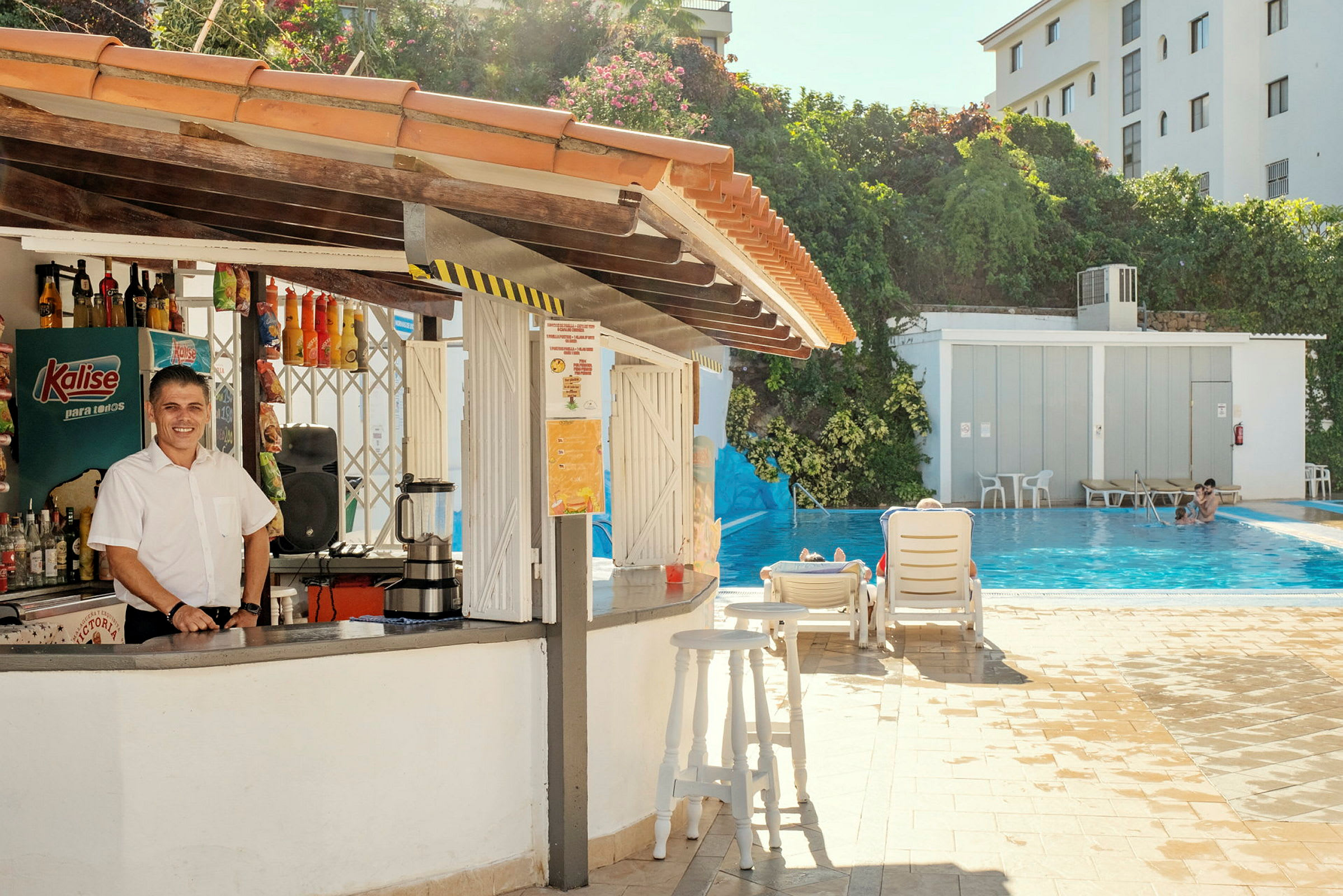 Udendørsbar ved en pool med liggestole og grønne omgivelser i baggrunden. (AI-genereret tekst)