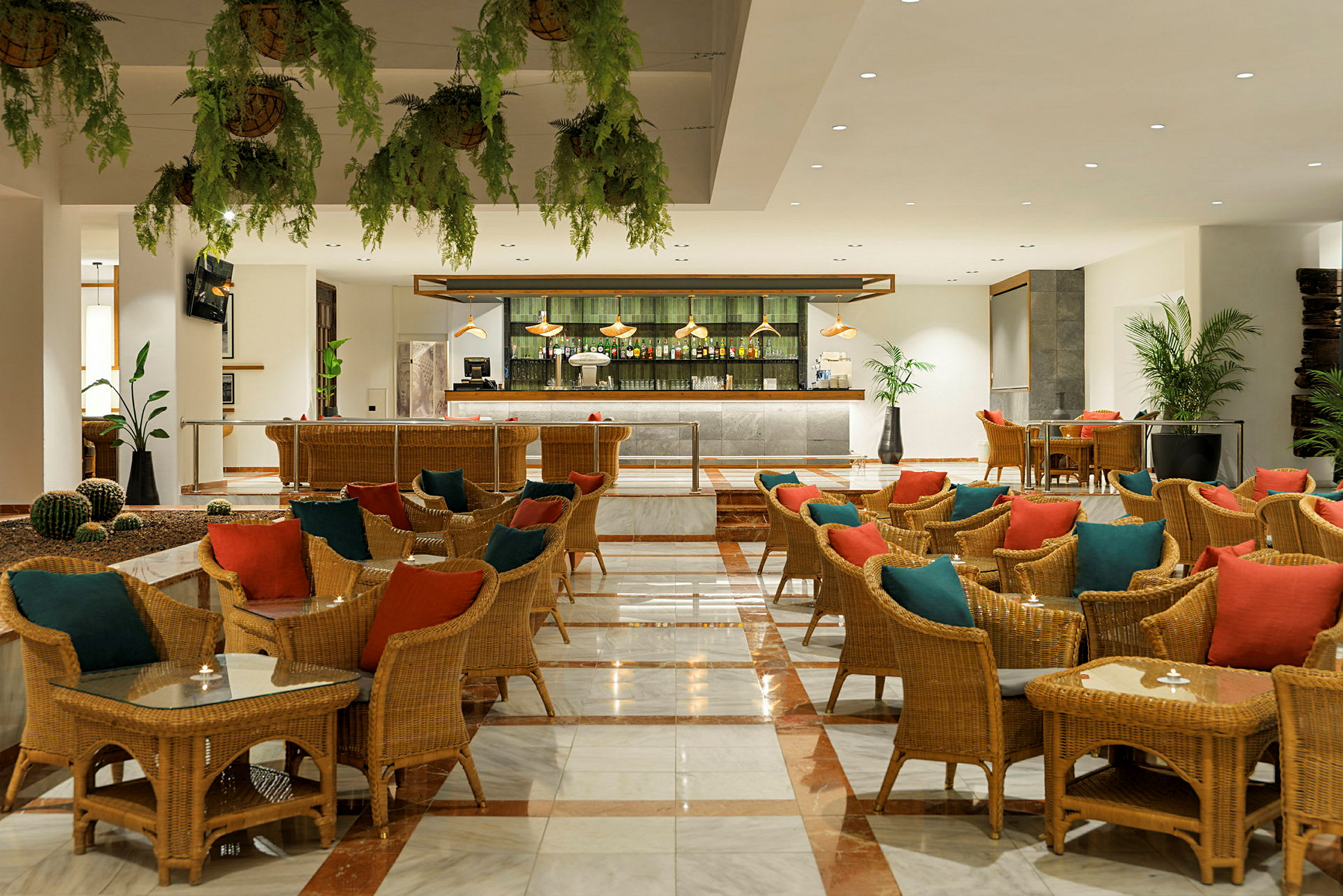 Restaurant eller loungeområde med flettede stole, borde og farverige puder samt en bar i baggrunden. (AI-genereret tekst)