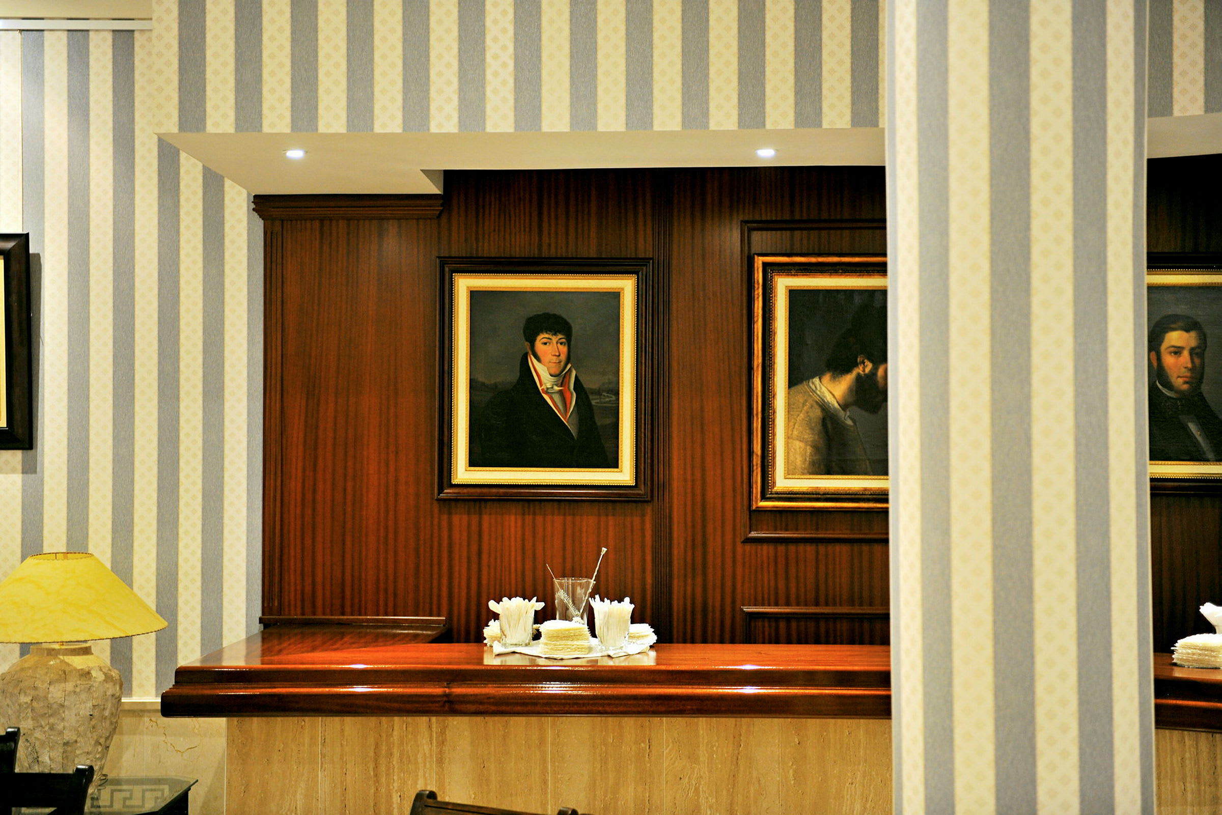 Indendørsbillede af en reception med træpaneler og malerier på væggen. Et bord er dekoreret med servietter og glas. (AI-genereret tekst)